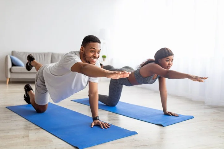 Fit-black-couple-stretching-their-arms-and-legs,-doing-yoga-or-pilates-on-mat-indoors.-Stay-home-hobbies-1325282150_727x484.jpeg
