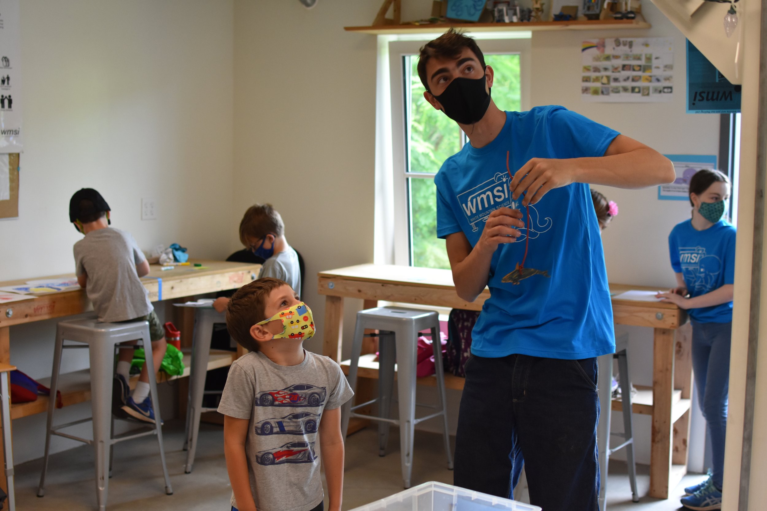  A WMSI Blue Shirt helps a student hang up a paper creation 