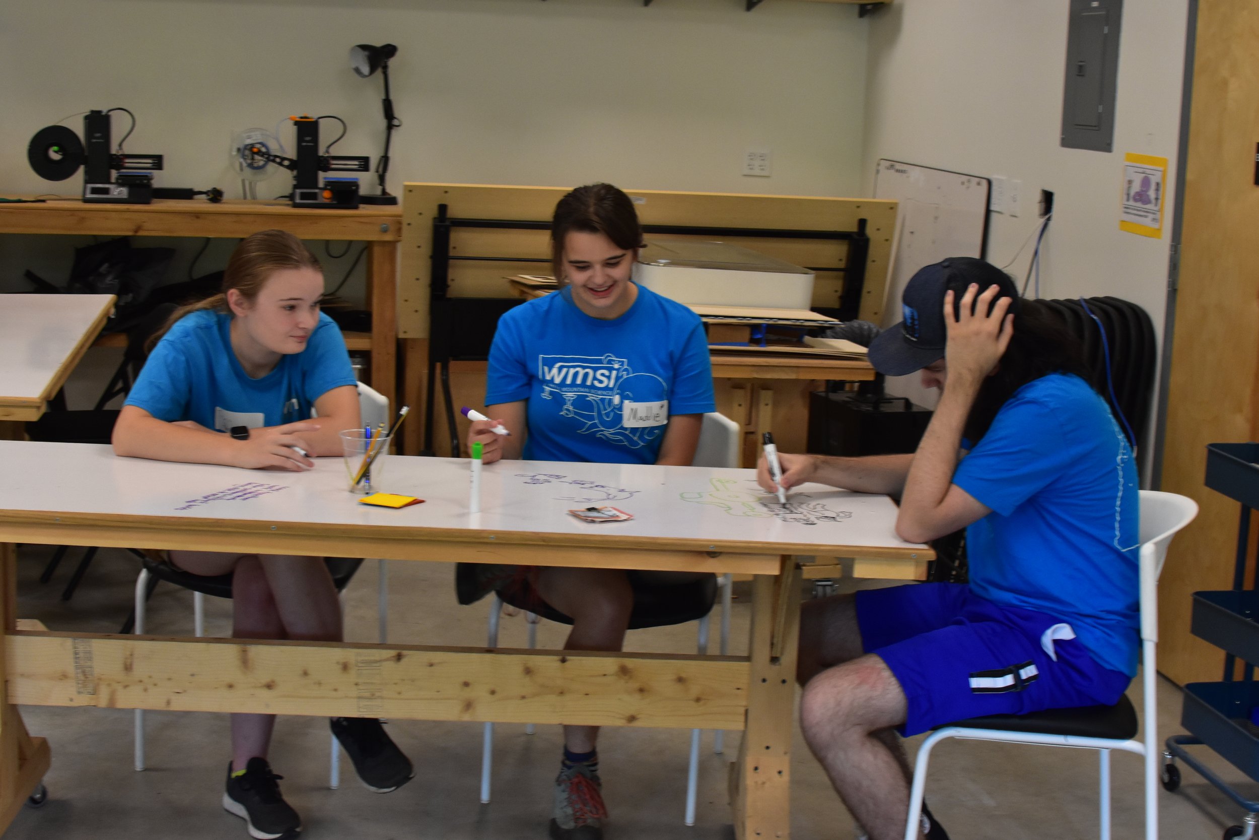  3 WMSI Blue Shirts discuss at a table 