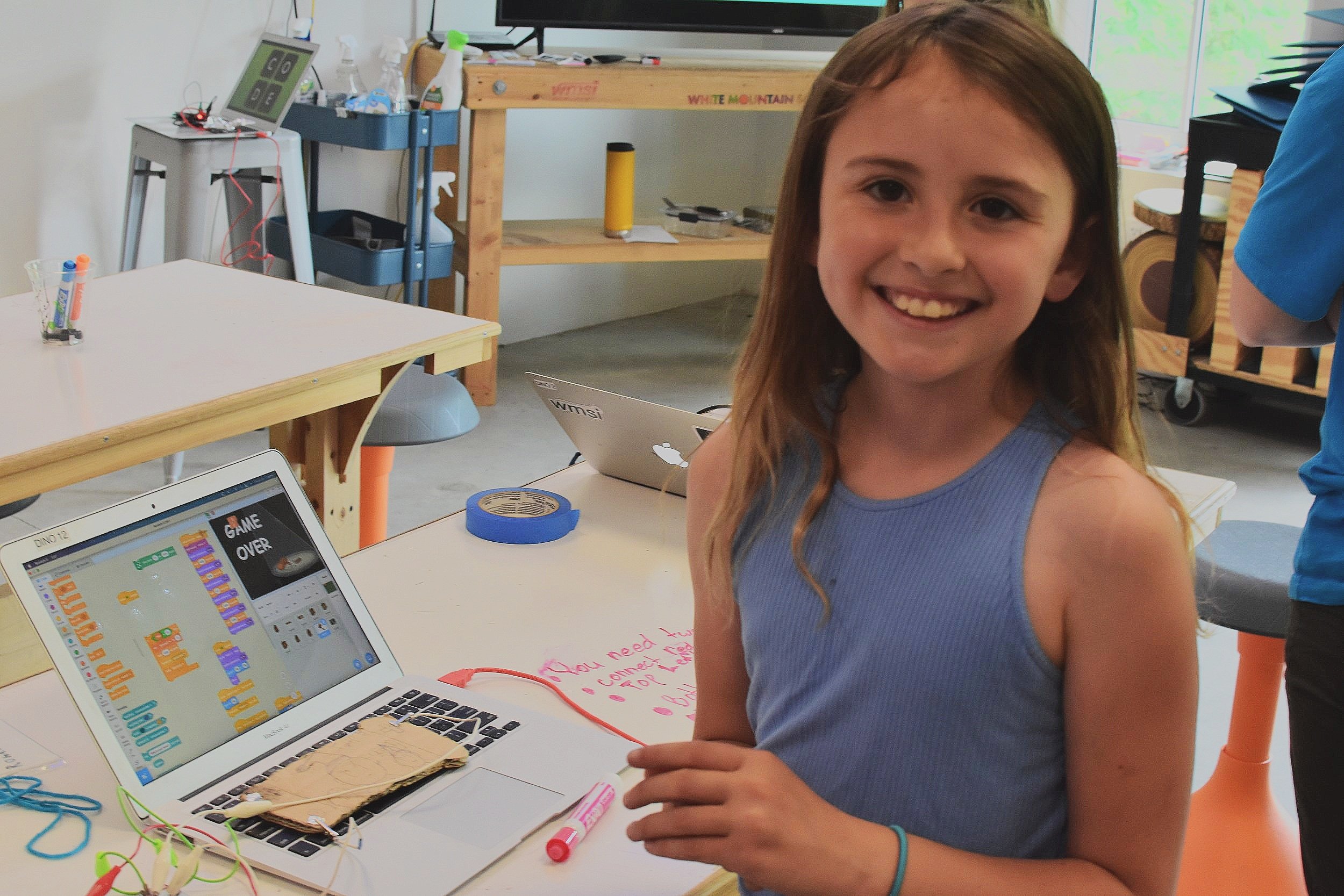  Student smiles in front of a computer with a scratch game on the screen 