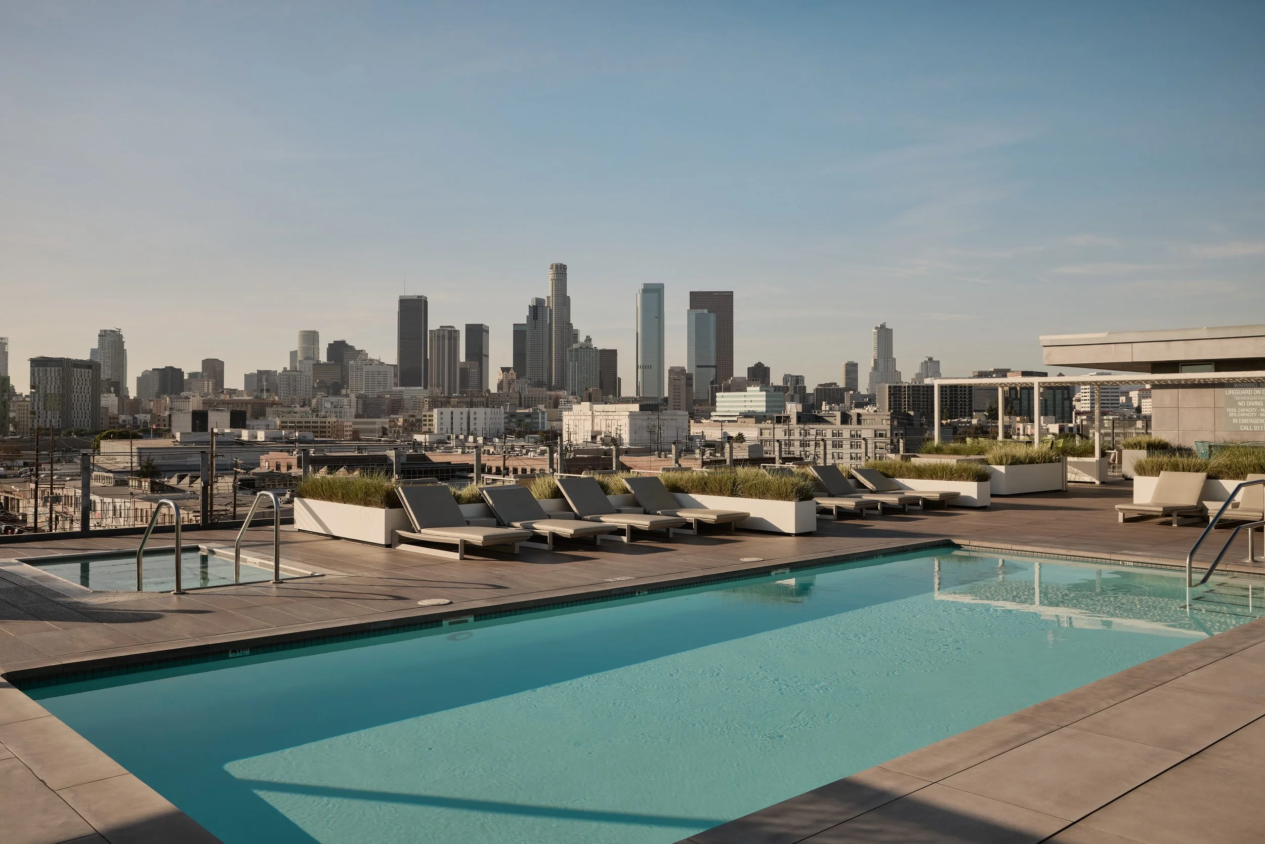 Barker Block rooftop amenities featuring a heated pool, lounge seating, and sweeping skyline views across downtown Los Angeles.