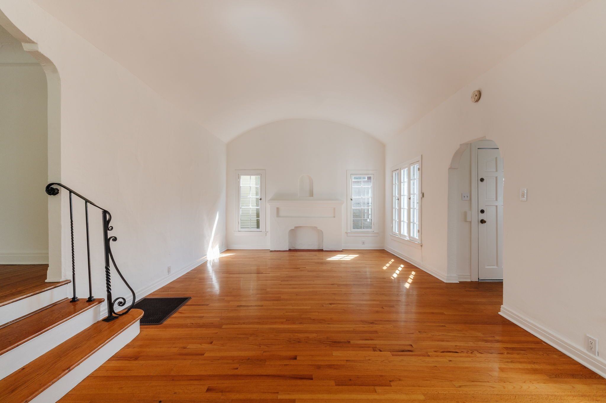 Bungalow living room with curved ceilings, wood floors, original windows, and a decorative mantel.