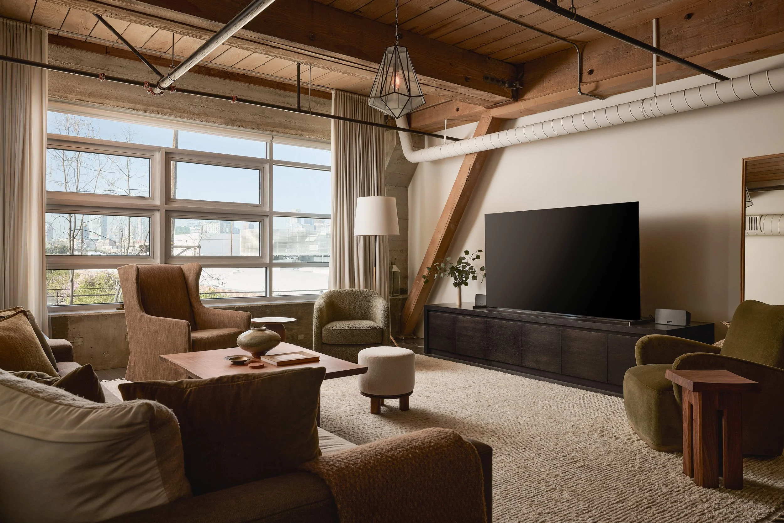 Arts District loft seating area by large industrial windows with floor-to-ceiling drapery and downtown skyline view.