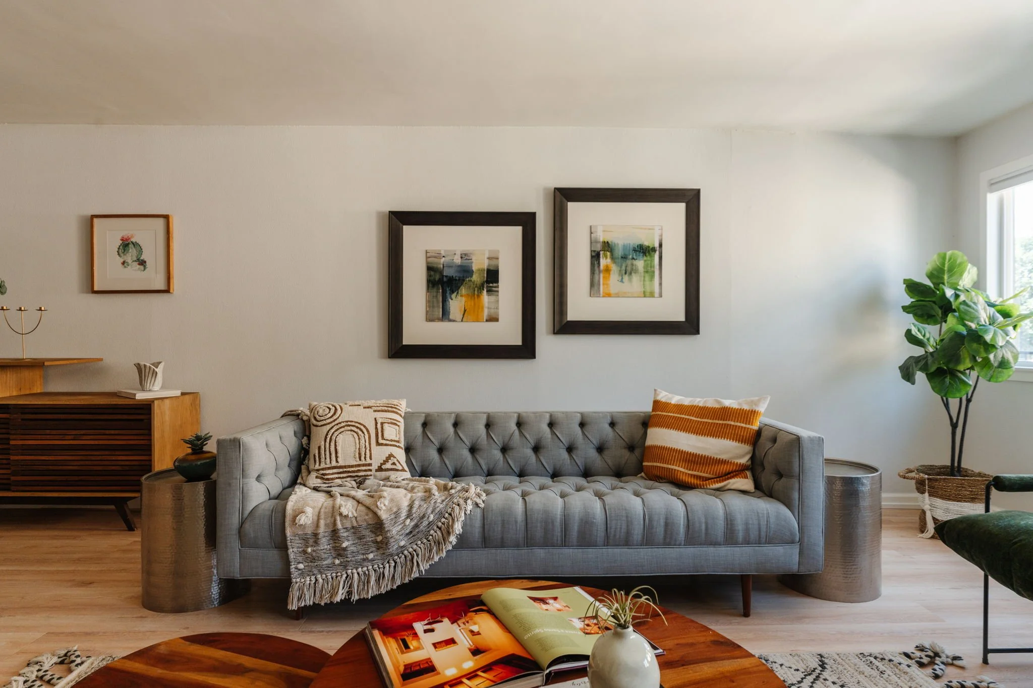 Living room with a tufted gray sofa, wood coffee tables, and natural light at 1559 Winona Blvd, Unit F2.