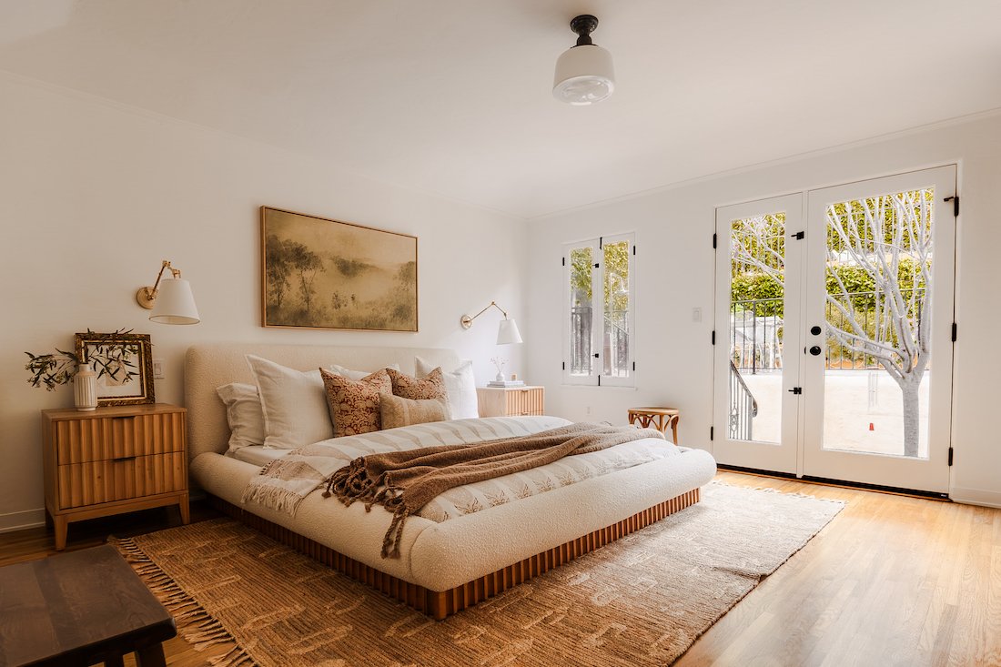 Primary bedroom with wood floors, custom finishes, abundant natural light, and French doors opening to the outdoor spaces for seamless indoor-outdoor living.