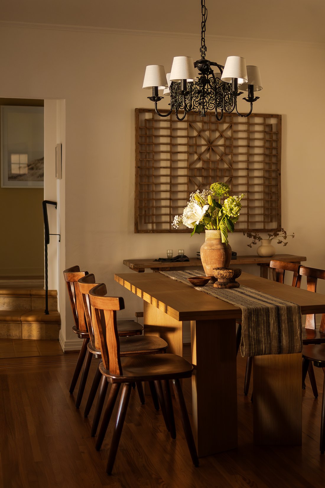 Formal dining room with warm natural light, original wood floors, wrought iron chandelier, and an elegant connection to the kitchen and main living areas.
