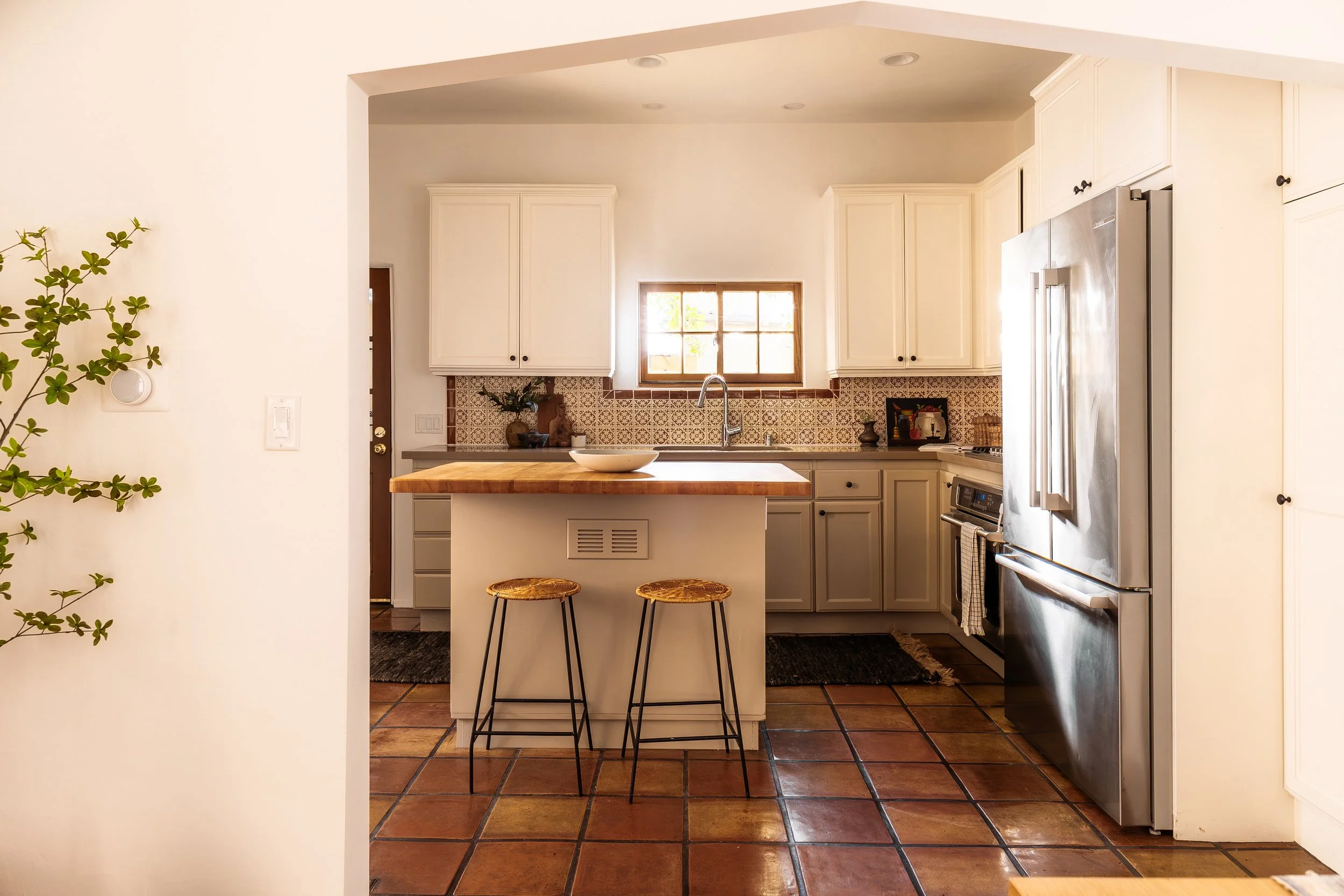 Updated chef’s kitchen with patterned tile backsplash, center island with seating, stainless steel appliances, and terracotta tile floors blending modern convenience with Spanish charm.