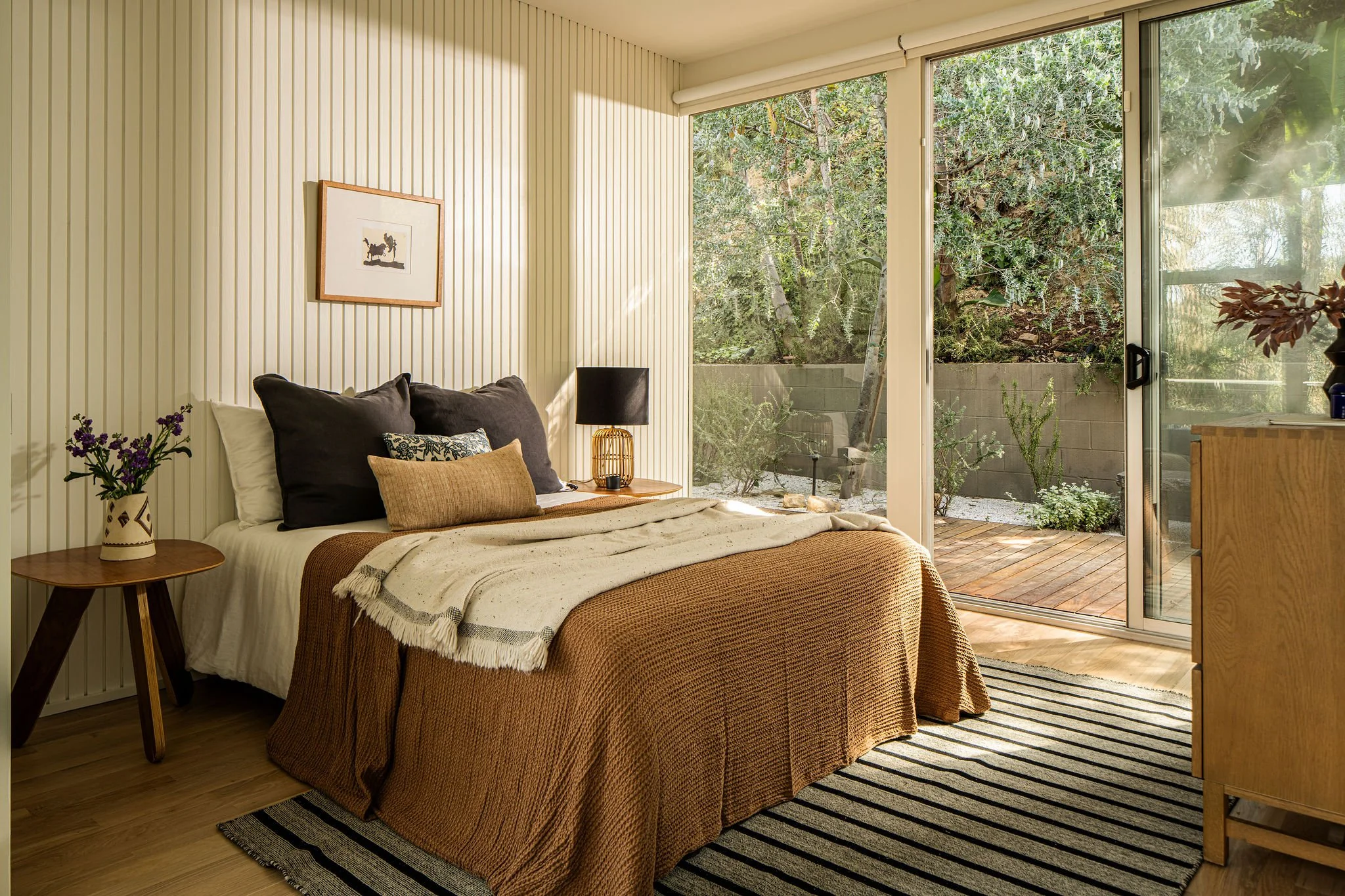 Mid-century modern bedroom with sliding glass doors opening to private garden patio Caption: Bedrooms maintain a strong connection to the outdoors, with direct access to private garden spaces.