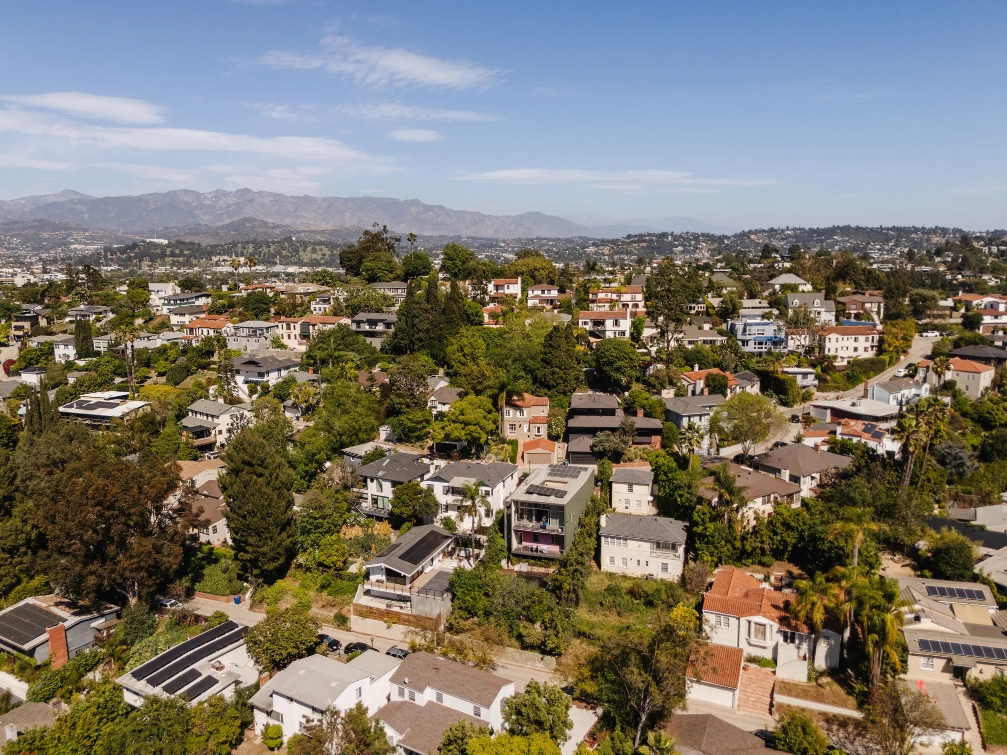 Daytime aerial view of Silver Lake residential streets and hillside homes with San Gabriel Mountains in the background