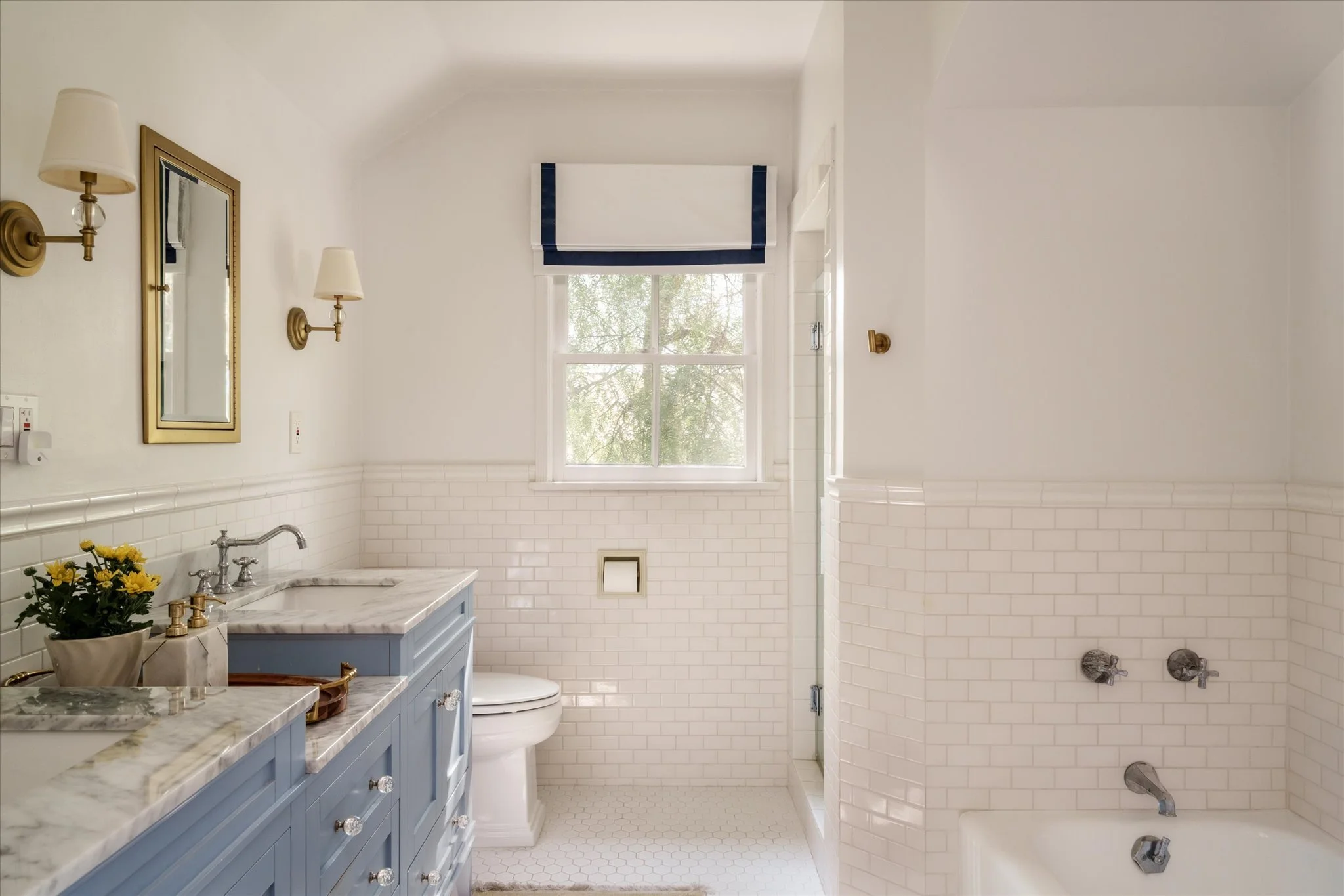 Remodeled primary bathroom with marble countertops, dual vanities, white tile and bathtub at the Glendale Colonial Revival home.