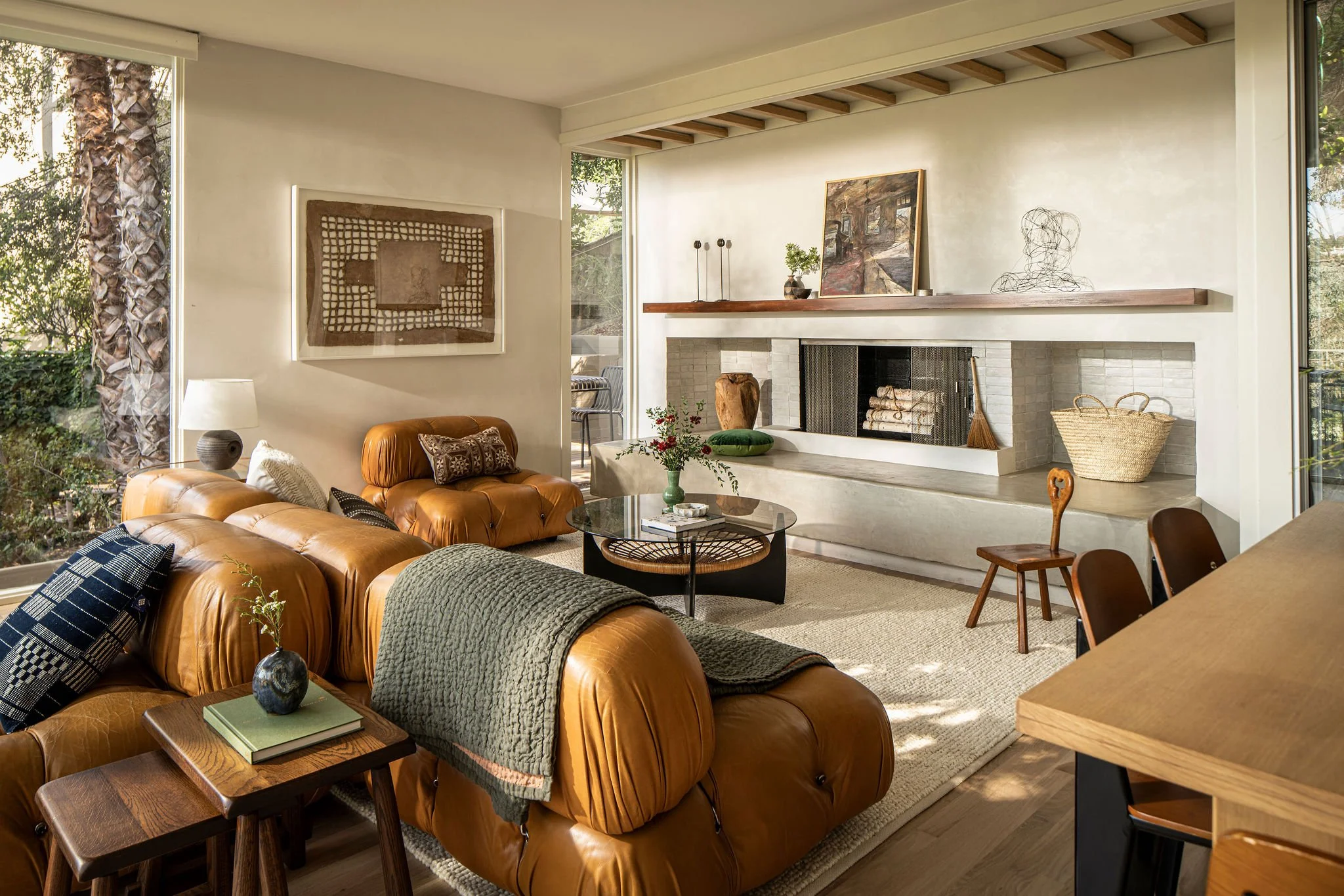 Post-and-beam living room with fireplace and glass walls in Hollywood Hills mid-century home Caption: The living room is anchored by a minimalist fireplace and framed by glass, capturing natural light throughout the day.