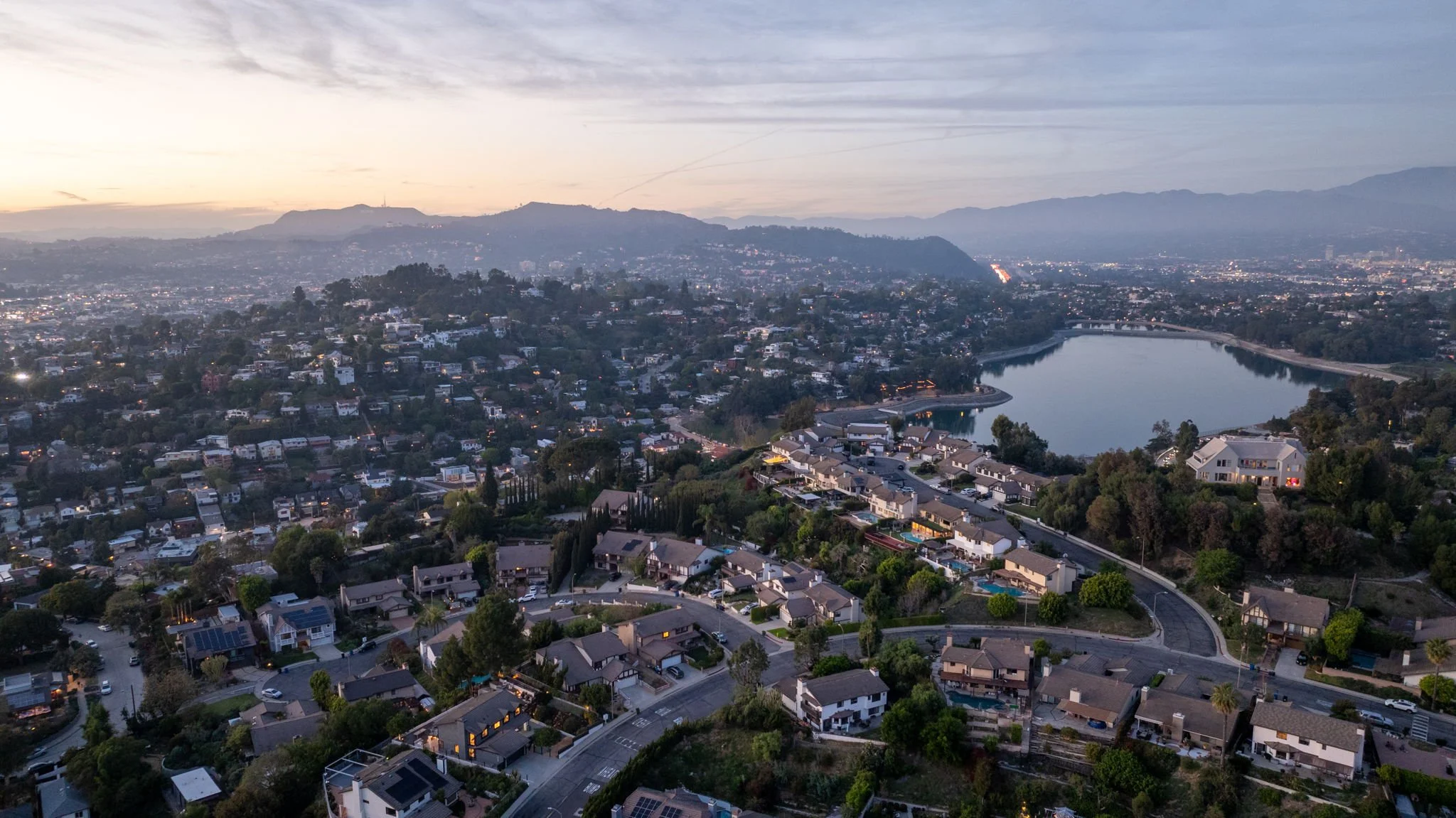 Aerial view of Silver Lake neighborhood and reservoir at dusk with Hollywood Hills in the background