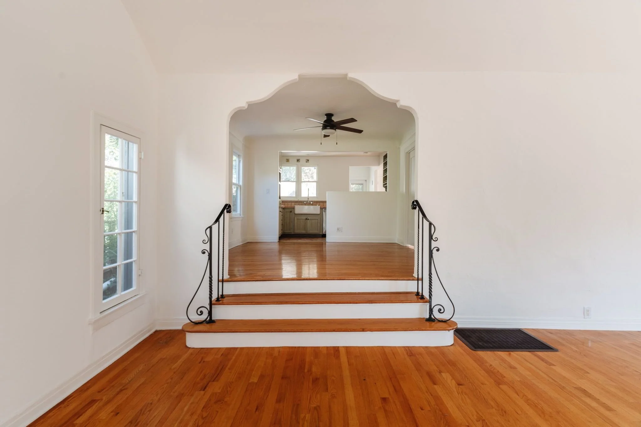 Shaped archway and wood steps with decorative iron railings connecting the bungalow’s living and dining rooms.