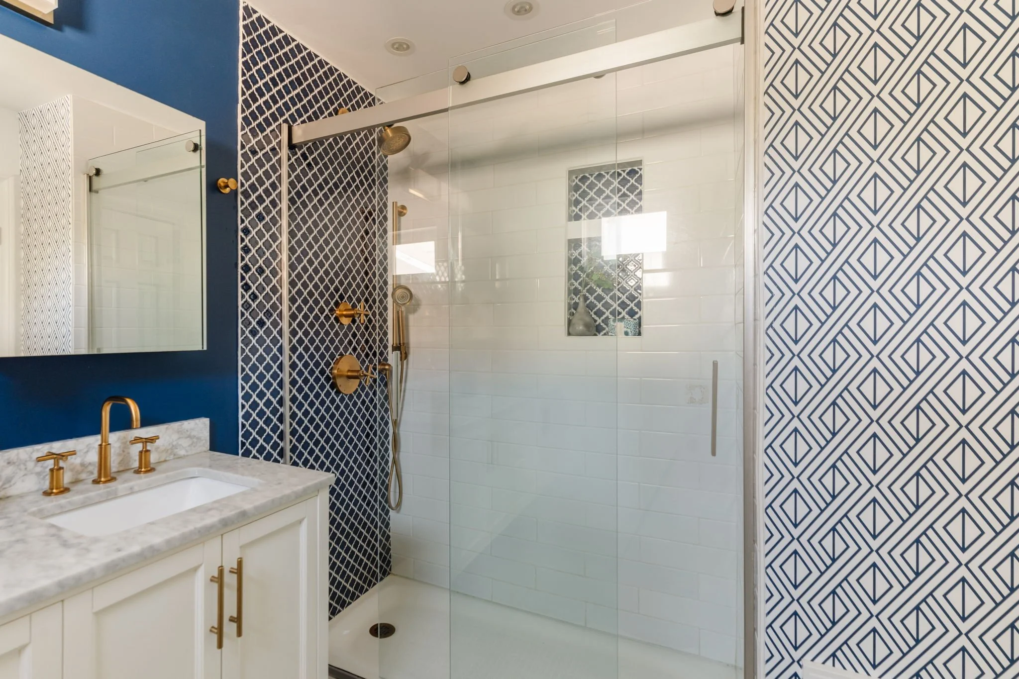 Remodeled bathroom with a glass-enclosed shower, blue patterned tile, and gold-toned fixtures.