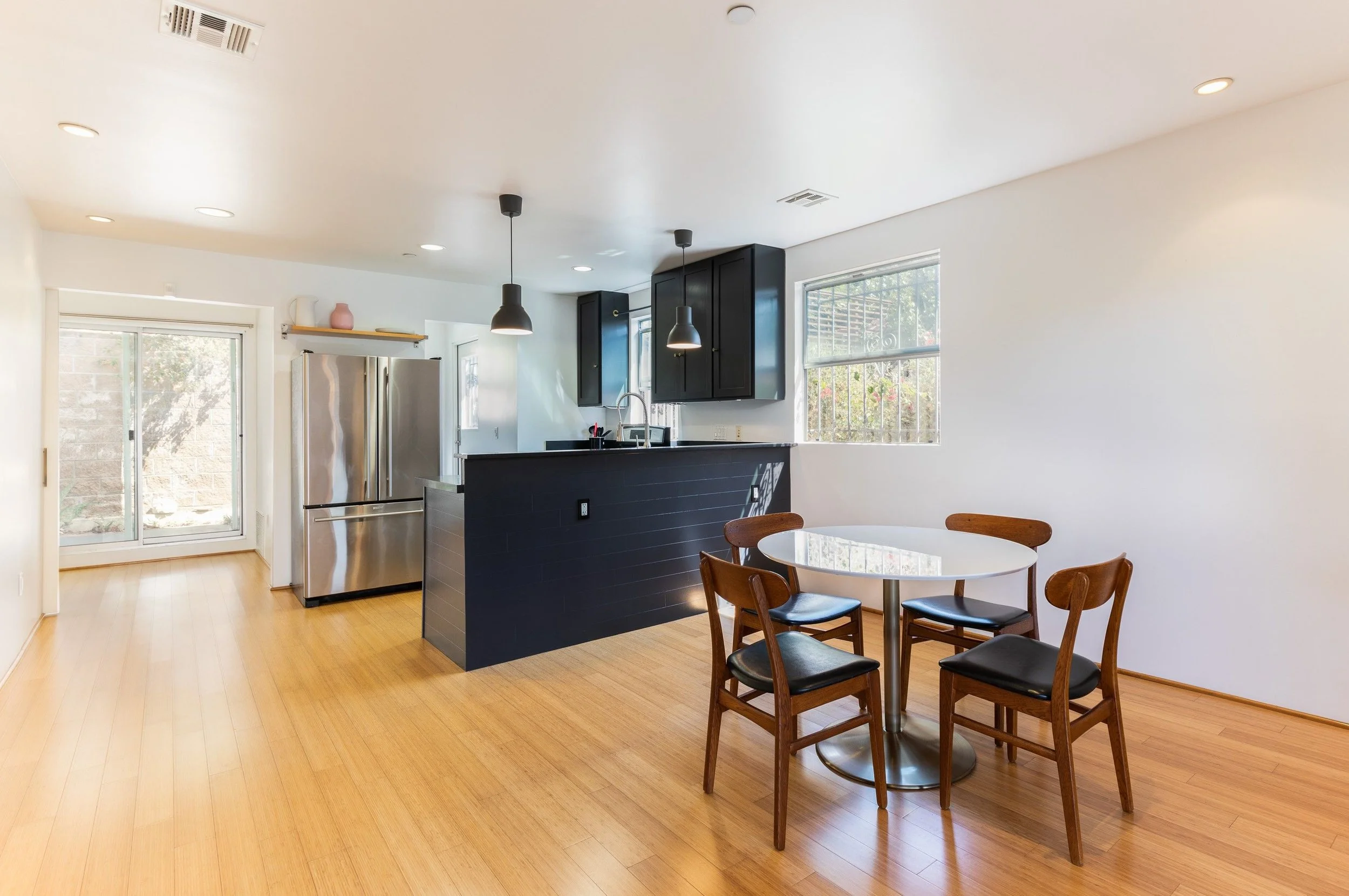 Kitchen and dining area with dark cabinetry, pendant lighting, light wood floors, and a round dining table.