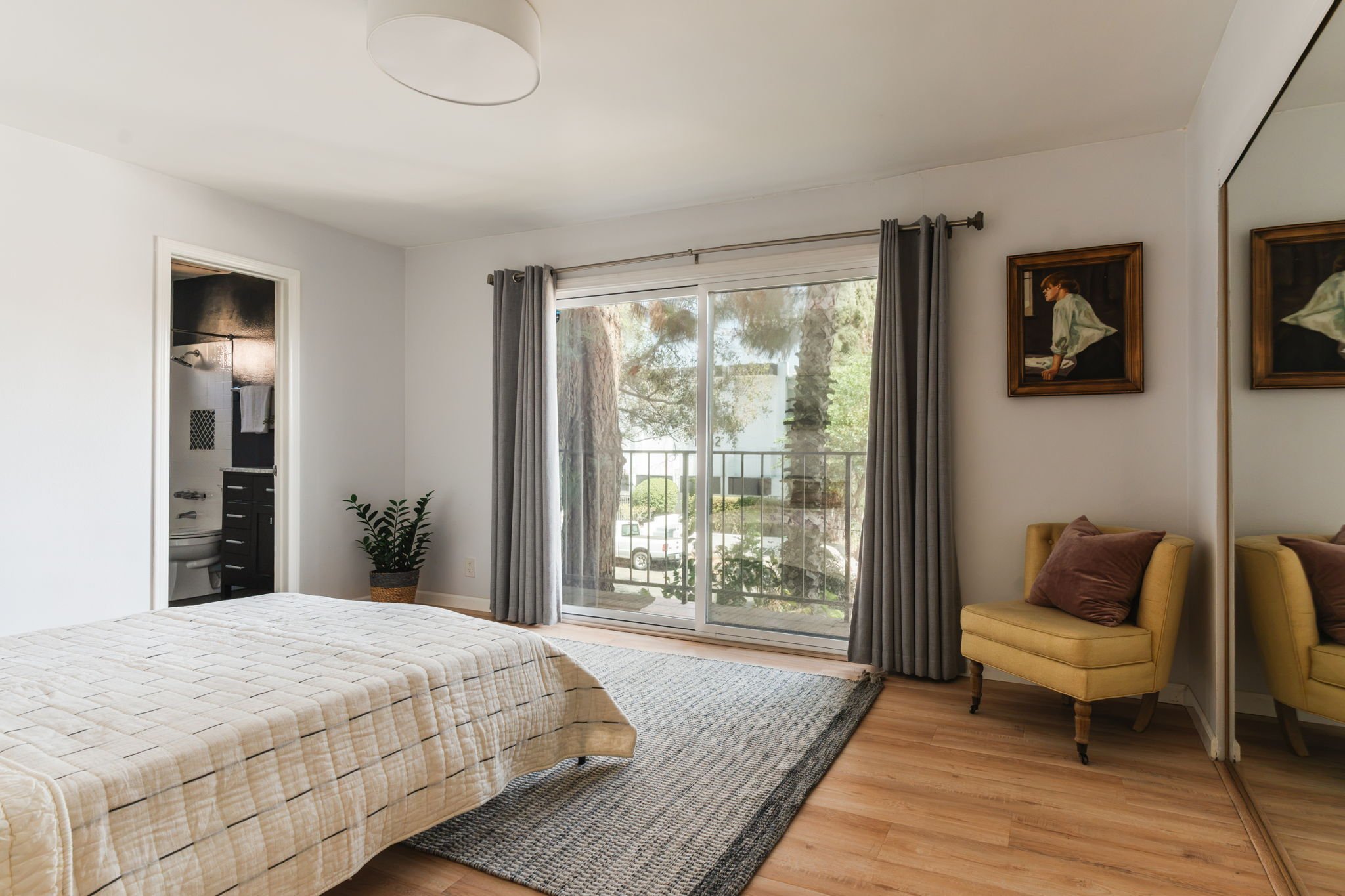 Bedroom with mirrored closet doors and sliding glass doors opening to the front patio overlooking trees.
