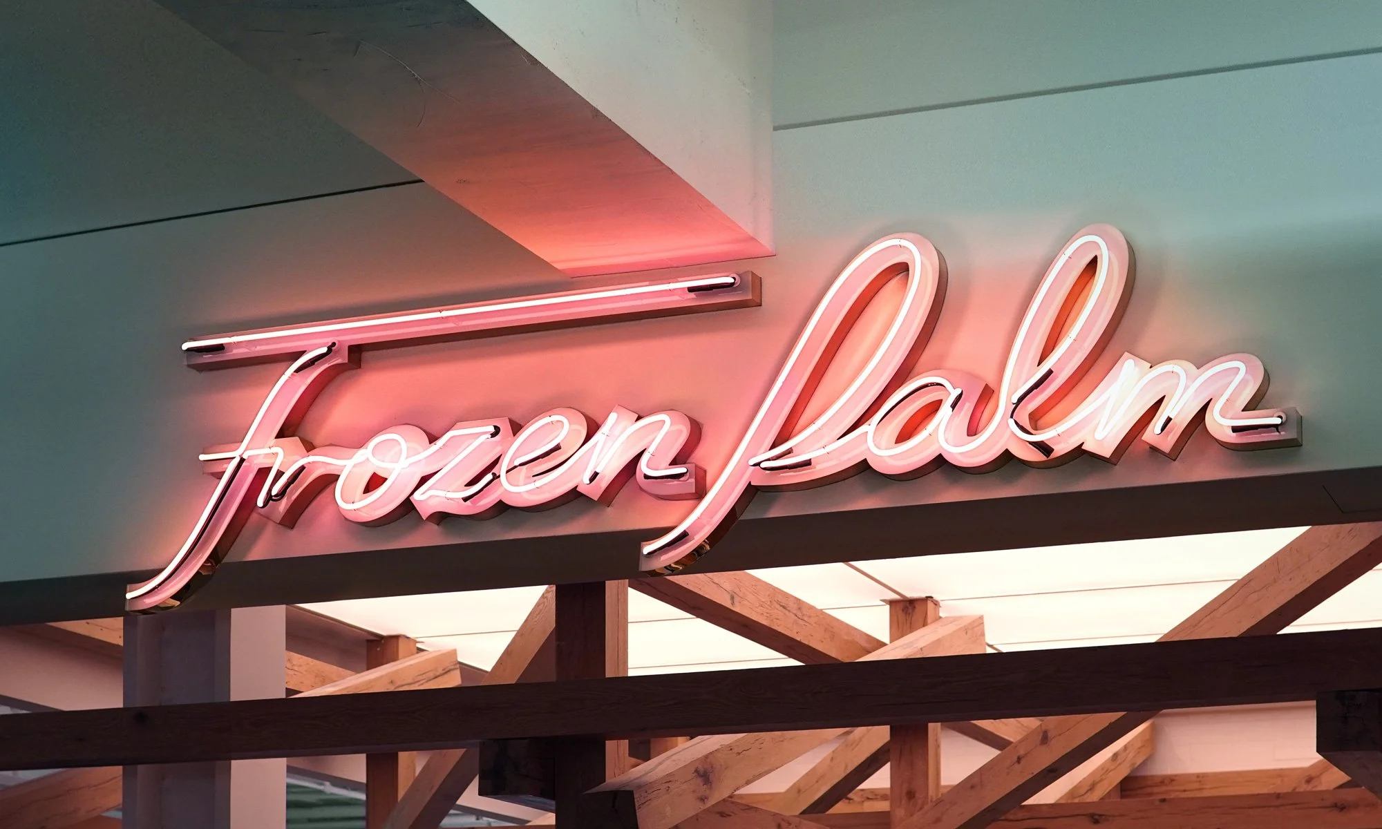 Neon sign displaying "Frozen Palm" with a pink glow, mounted on a wall with wooden structures.