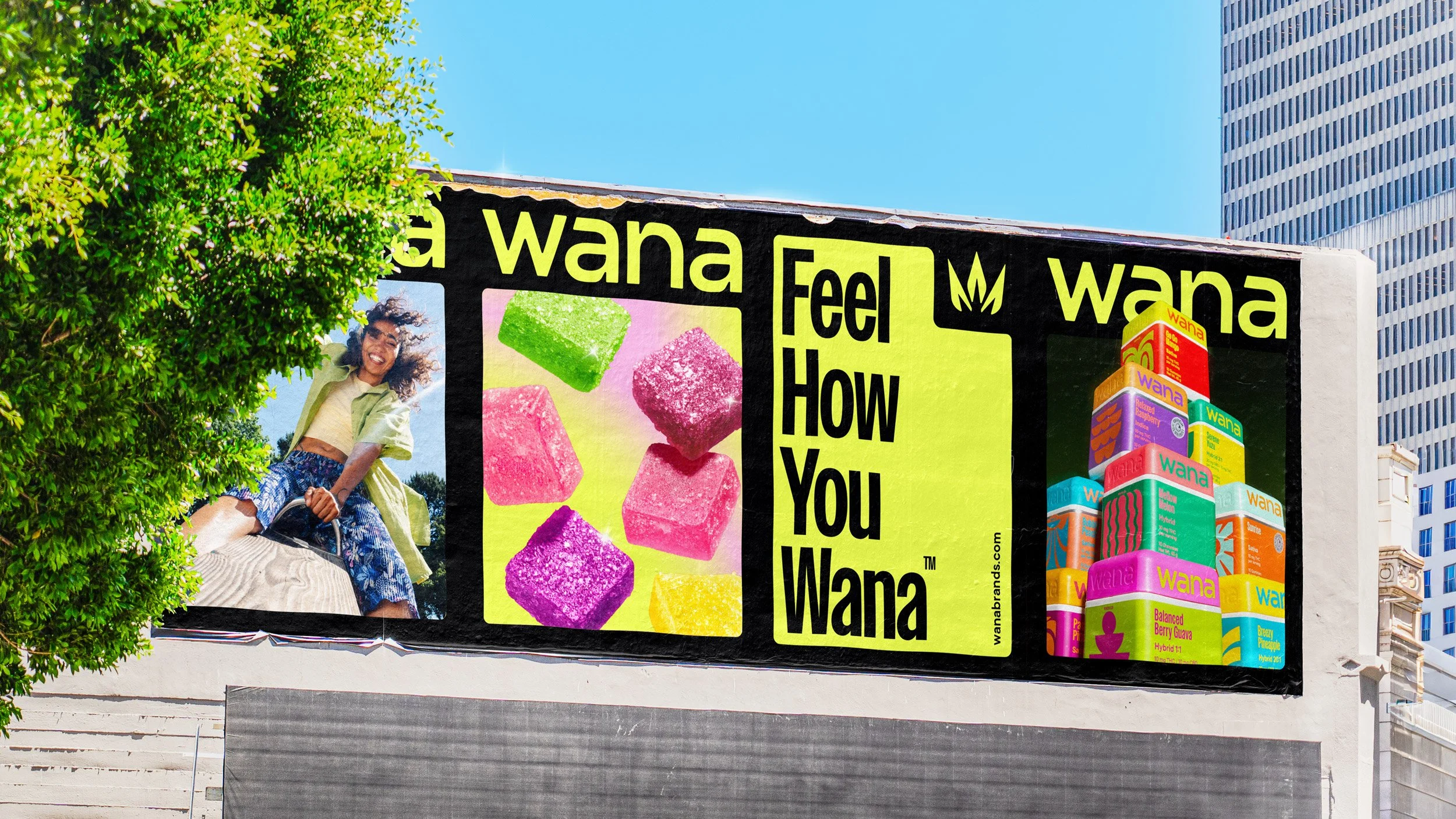 A colorful billboard advertisement featuring a smiling woman, brightly colored candy illustrations, and a stack of juice boxes with the word "Wana" on them, against a city skyline with tall buildings and a blue sky.