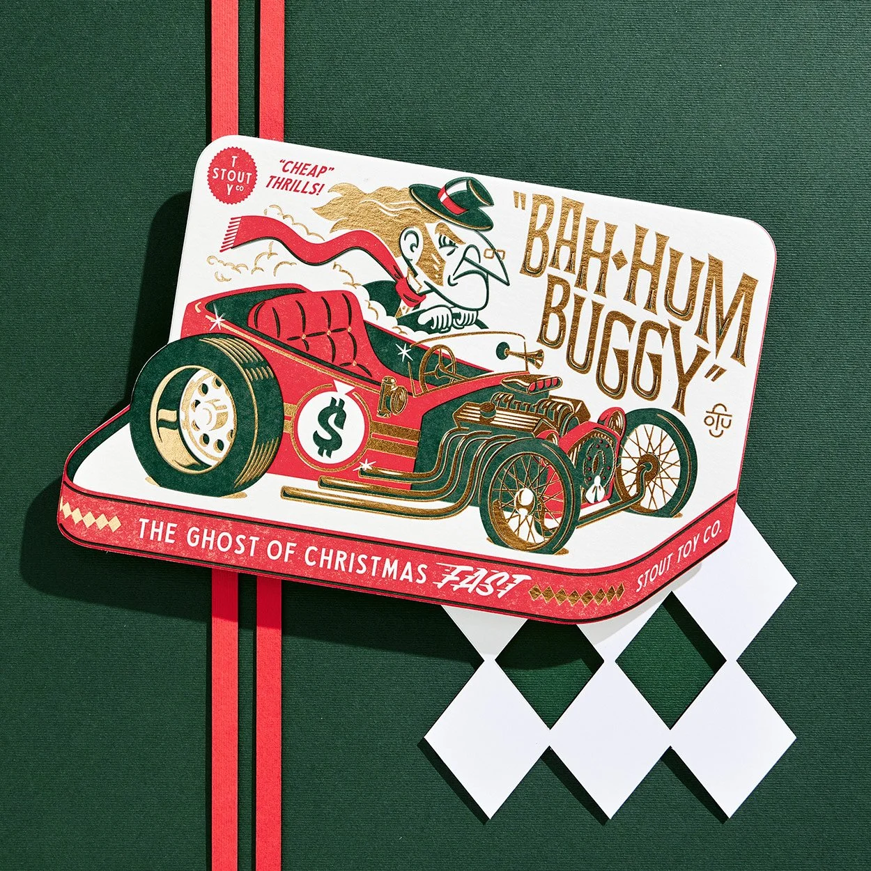 Illustration of a vintage-style racing car with a grumpy cartoon driver, labeled "Bah-Hum Buggy," on a green background. The car is red with dollar sign on the side and features text "The Ghost of Christmas Fast," "Cheap Thrills!" and "Stout Toy Co."