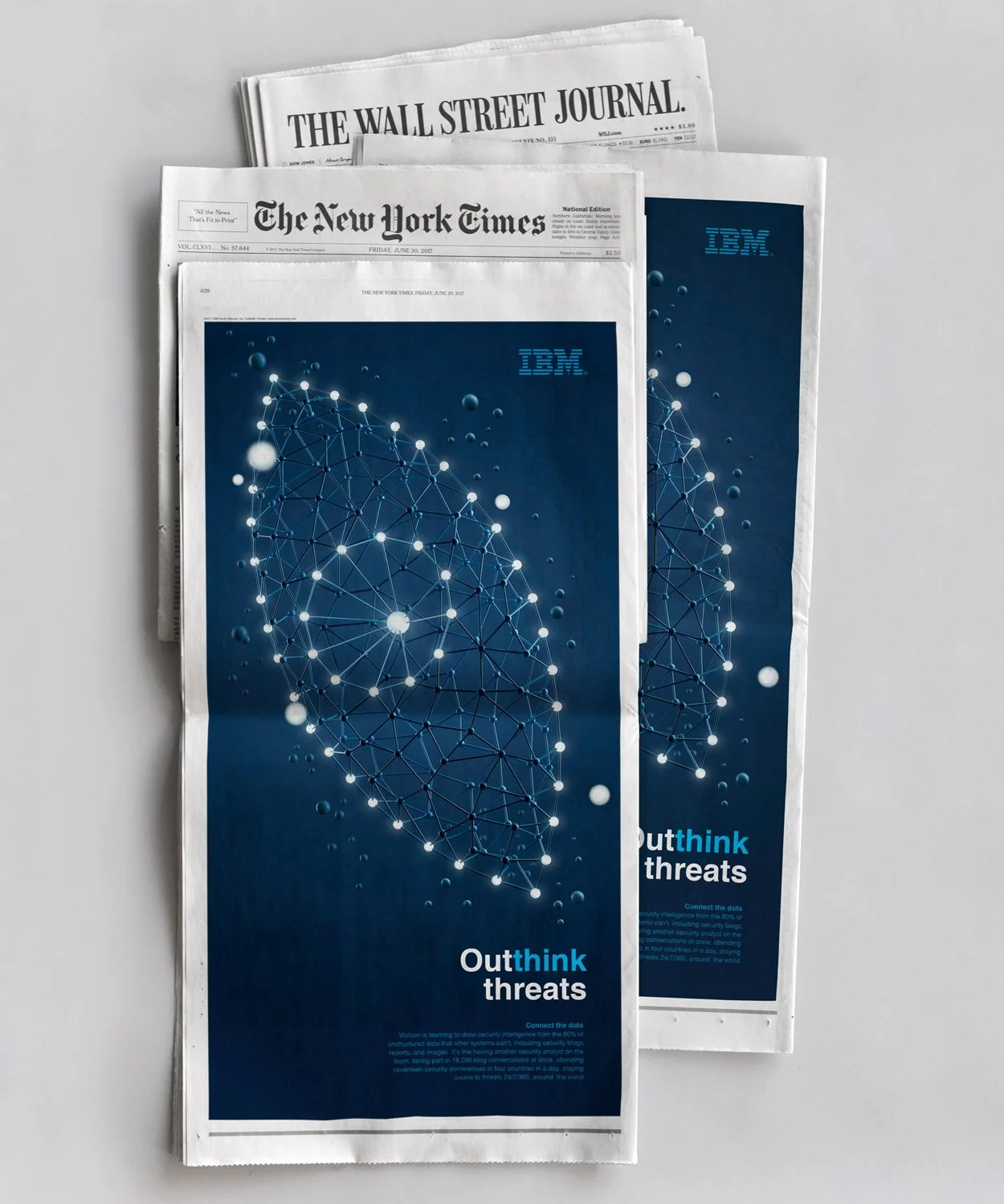 A stack of newspapers including The Wall Street Journal and The New York Times featuring an IBM advertisement with abstract network design and the text "Outthink threats."