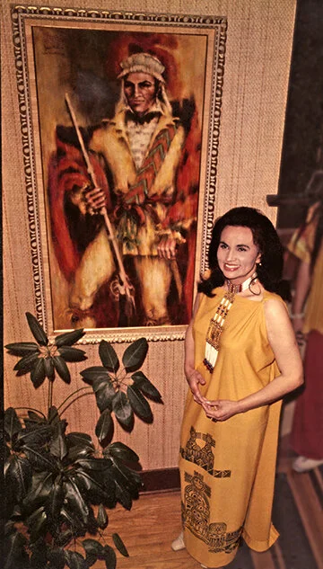 Joan Hill poses in front of one of her paintings, a portrait of a 19th-century Muskogee leader in oil.