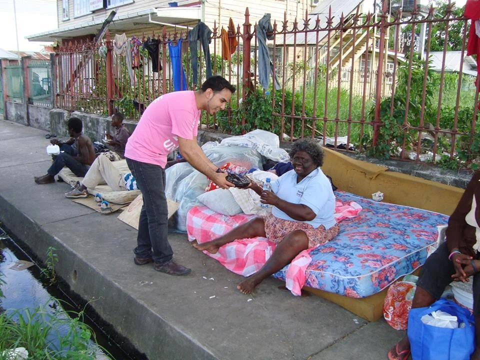 A Guyana Foundation volunteer handing over a hot meal to an individual living on the streets of Georgetown.