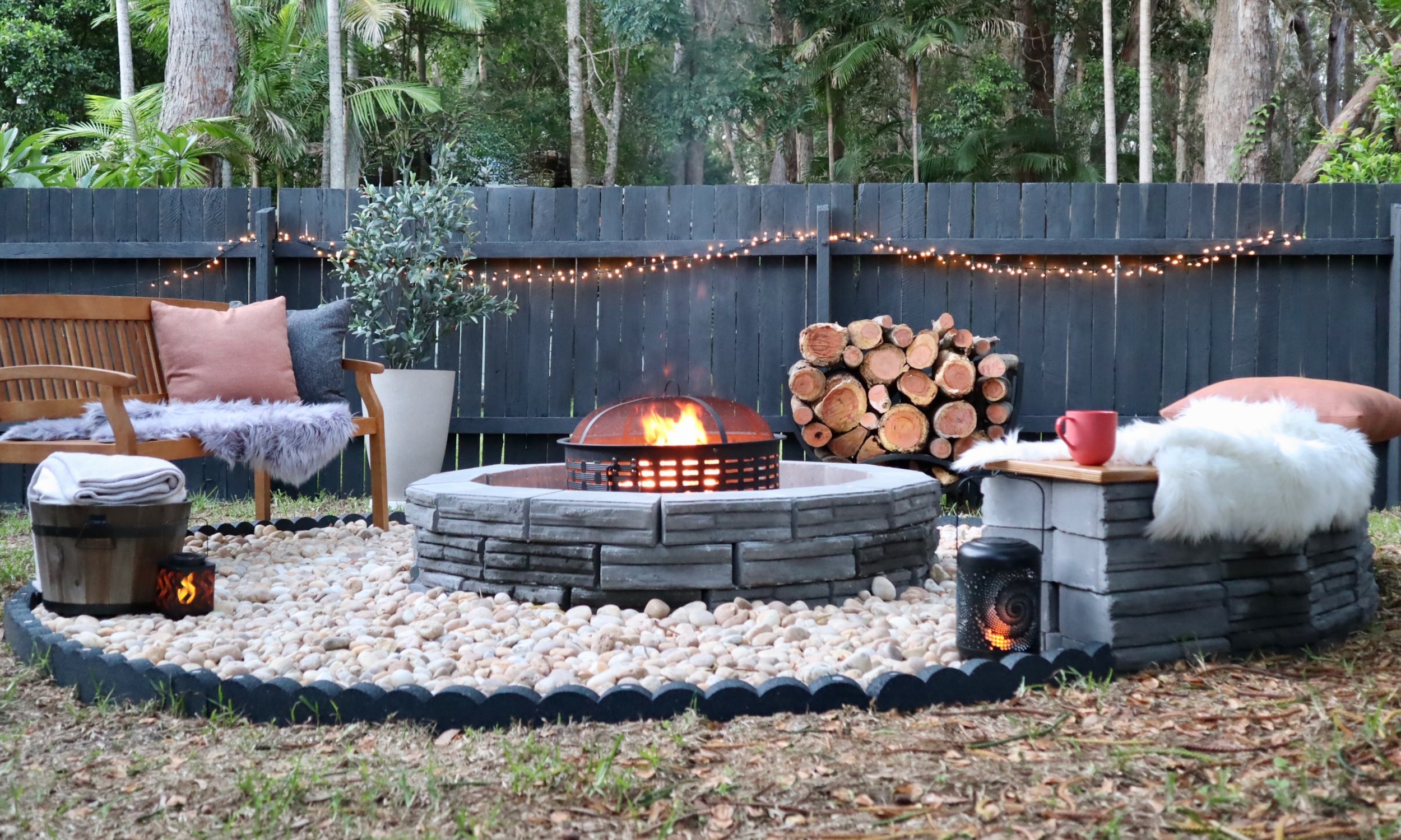 Outdoor fire pit area with seating, lights, and stacked wood