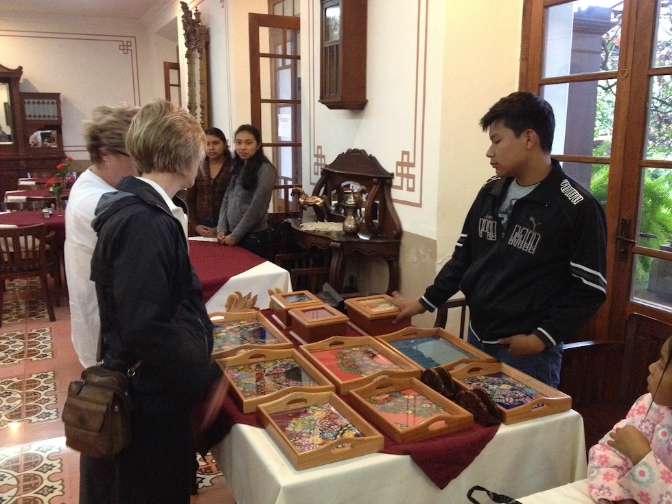 Roberto shows off the handcrafted wood-and-glass serving trays and keepsake boxes, with traditional huipil textiles.
