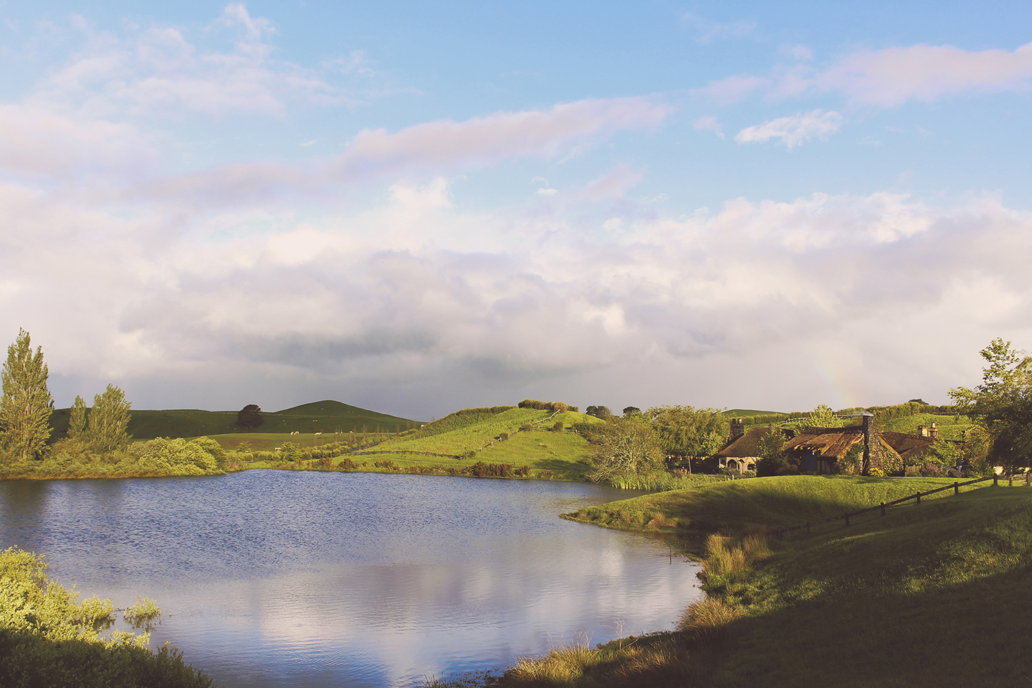 Retreating stormclouds and a rainbow over Hobbiton lake and the Green Dragon Inn.