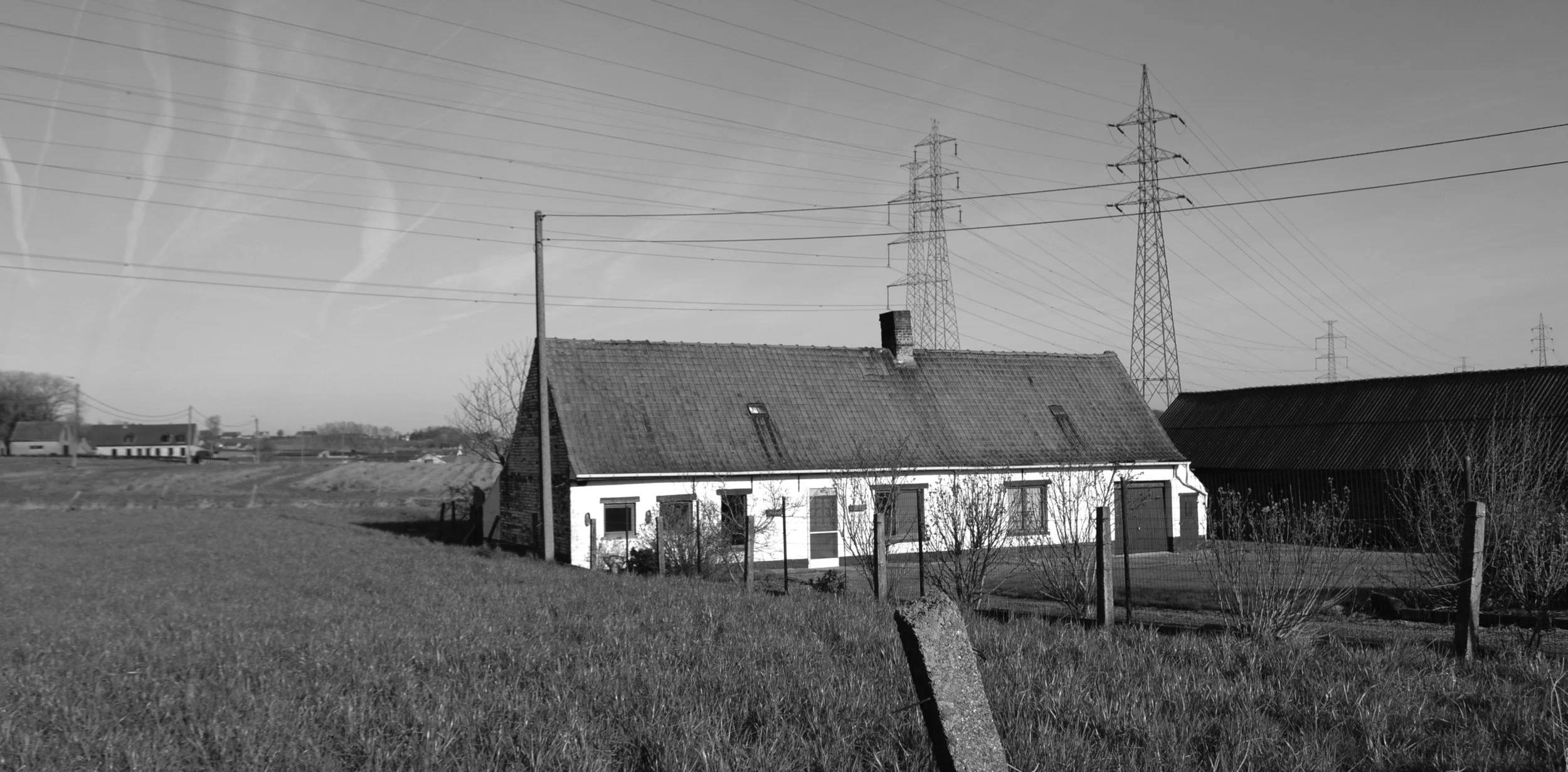 Een bestaande landelijke woning in slechte bouwfysische staat wordt afgebroken en vervangen door een energiezuinige nieuwbouwwoning in CLT. Het bouwvolume, materiaal en verschijningsvorm van de bestaande woning worden behouden om het vernaculaire aspect van de rurale architectuur te honoreren. Aan de straatzijde wordt het bestaande uitzicht -met zijn veelsoortige gevelopeningen- ingepast in de nieuwe gevel. Aan de achtergevel is er voor ruimere raampartijen gekozen om het zicht op het open landschap te maximaliseren.