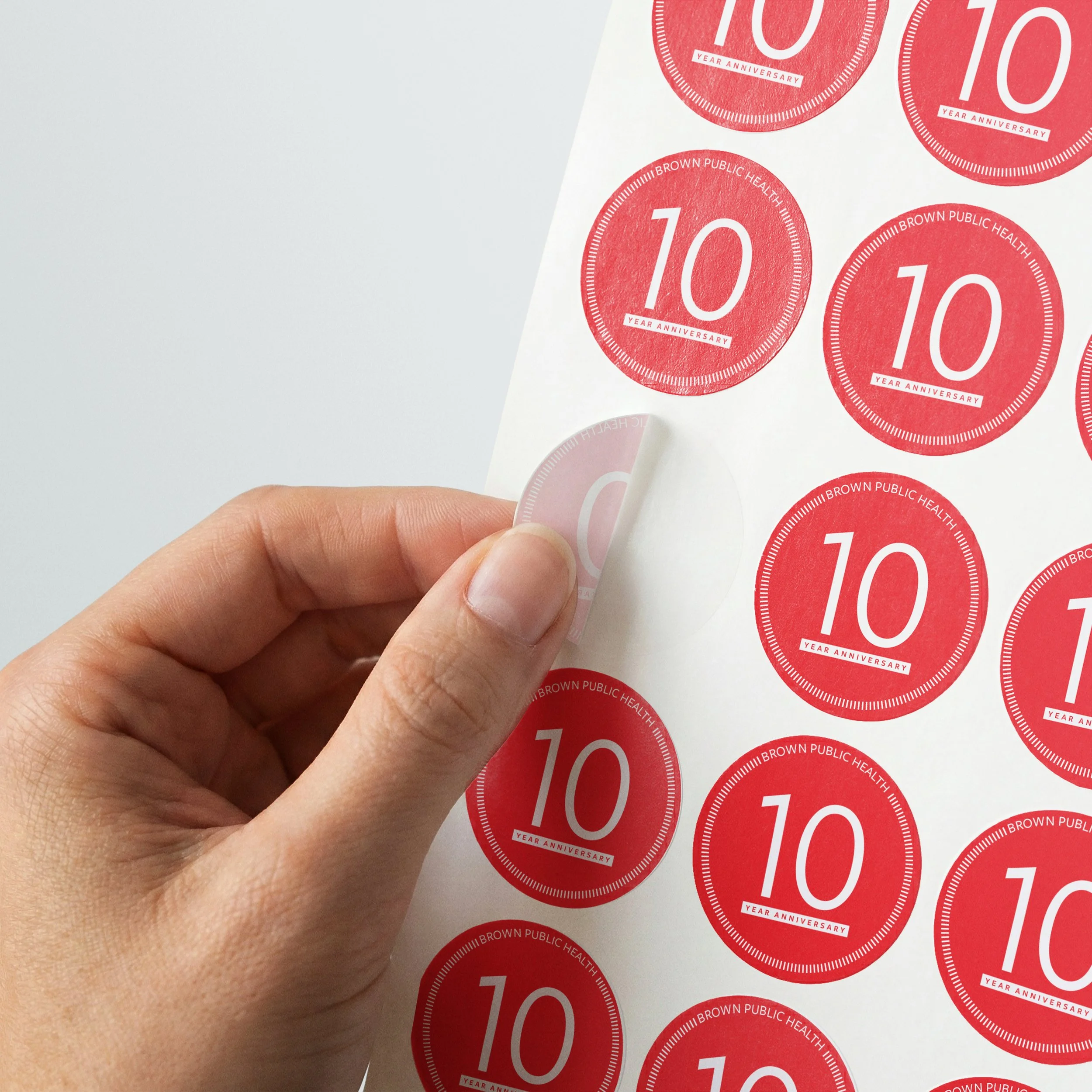 Hand peeling a sticker with the SPH 10 Year logo on it from a sheet