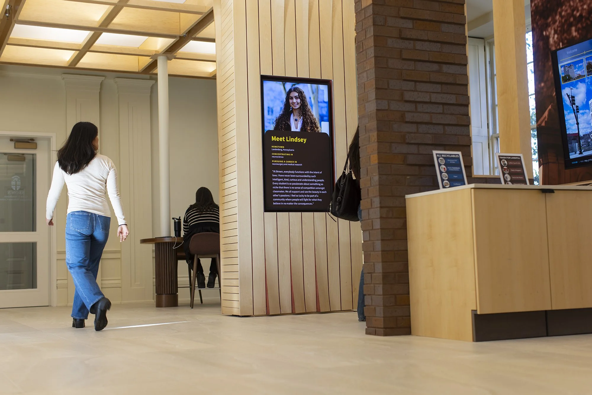 Person walking by a digital screen displaying a student profile