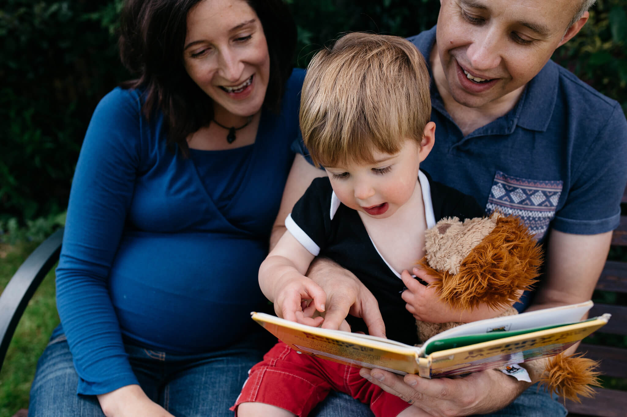 Pregnant mum with toddler son and dad reading a book