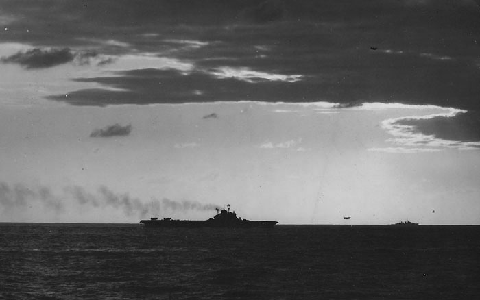 HMS VICTORIOUS launches aircraft. The low freeboard betrays this as one of the original three Illustrious class carriers, while the clearly silhouetted director in front of the island is a modification made to HMS VICTORIOUS and FORMIDABLE before the Sakishima operation. The position of the radar mast reveals this to be VICTORIOUS.