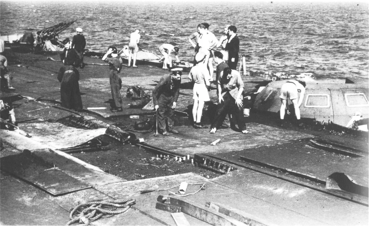 Damage control teams work on replacing the damaged plate steel alongside HMS VICTORIOUS' disabled B2 4.5in turret. The wrecked accelerator is clearly visible in the middle ground.