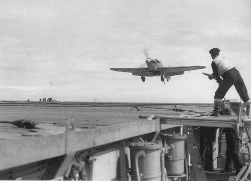 A signalman gives the 'cut engine' signal to an approaching Sea Hurricane.