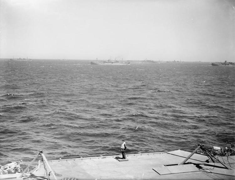 A deck officer observes flight activities with the Pedestal convoy in the background.