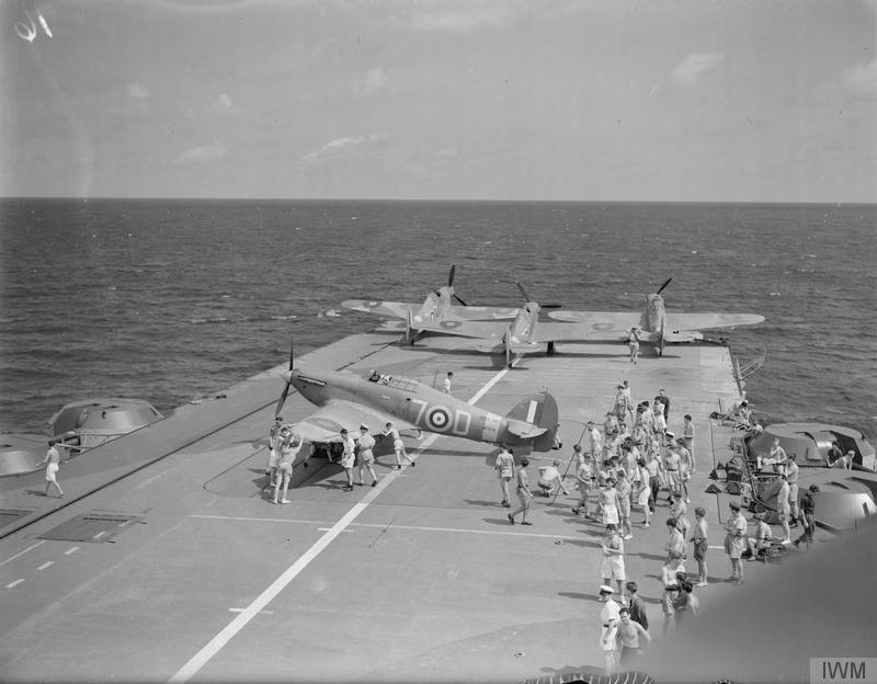 Deck crew position a non-folding Sea Hurricane on HMS INDOMITABLE's large forward lift. They had to be skewed sideways onto roller-rails to arrange them within the hangar.