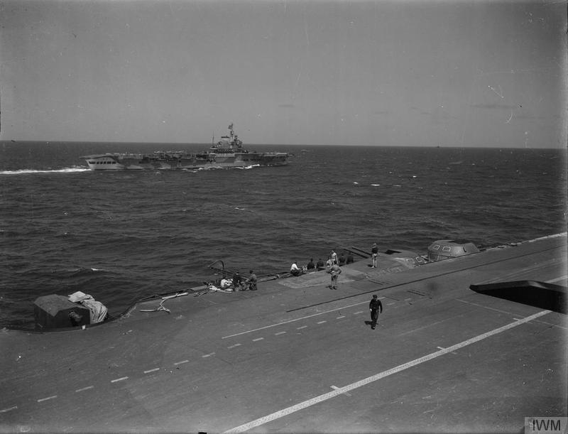 While the original caption states this is HMS VICTORIOUS as seen from the island of INDOMITABLE during Operation PEDESTAL, the identities are likely the other way around. (Only VICTORIOUS had the raised deck faring behind the 4.5in turrets, seen here with crew standing on it)