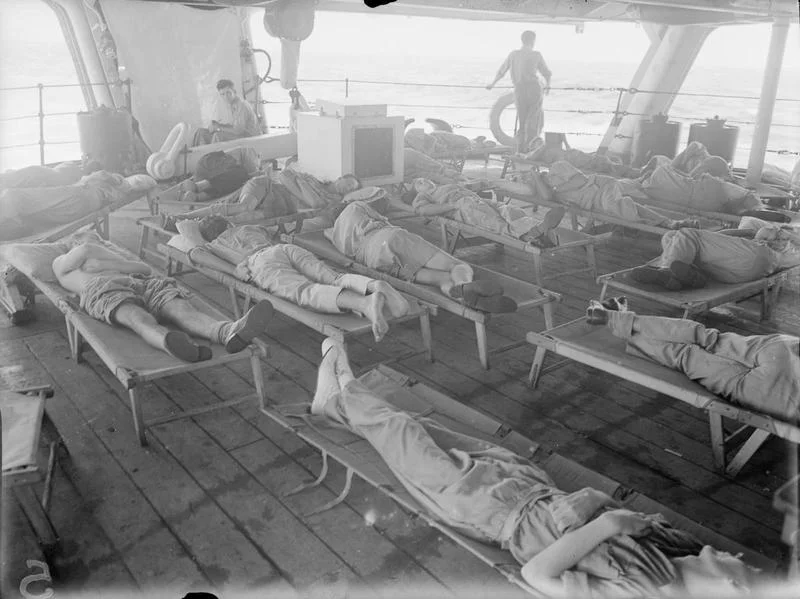 Fleet Air Arm pilots and observers sleep on camp beds on the quarterdeck of HMS Illustrious to catch what cool sea air they can during the Andaman Island operation.