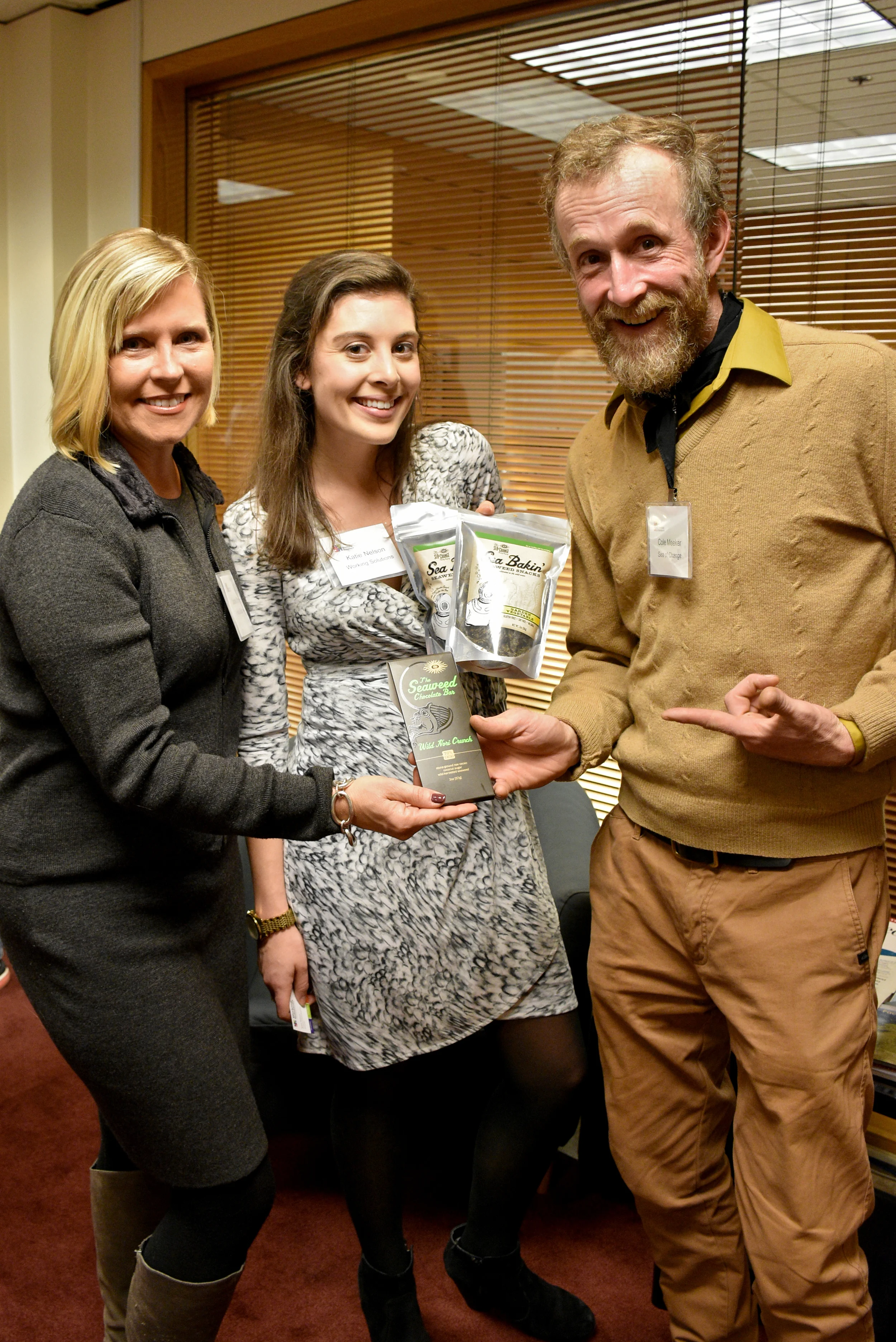 Cole Meeker of Sea of Change Trading Company shows off his seaweed snacks and seaweed chocolate bar to Working Solutions Director of Business Development Laurie O'Hara and Marketing & Development Associate Katie Nelson