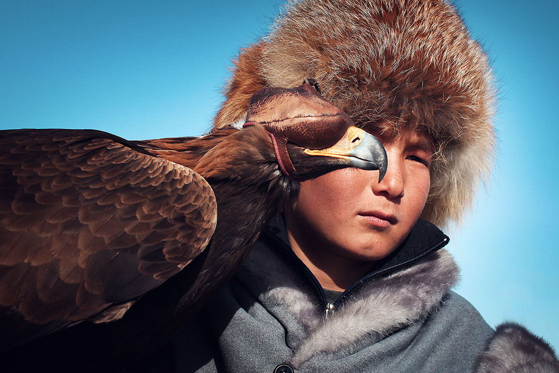 A young Kazakh falconer. His eagle’s eyes are covered by a tomoro, a leather mask intended to keep it from feeling stressed or recklessly attacking anyone / Jeune aiglier kazakh. Son rapace a les yeux recouverts d’un tomoro , un masque en cuir pour l’empêcher de stresser et d’attaquer sans discernemen | KAZAKHSTAN