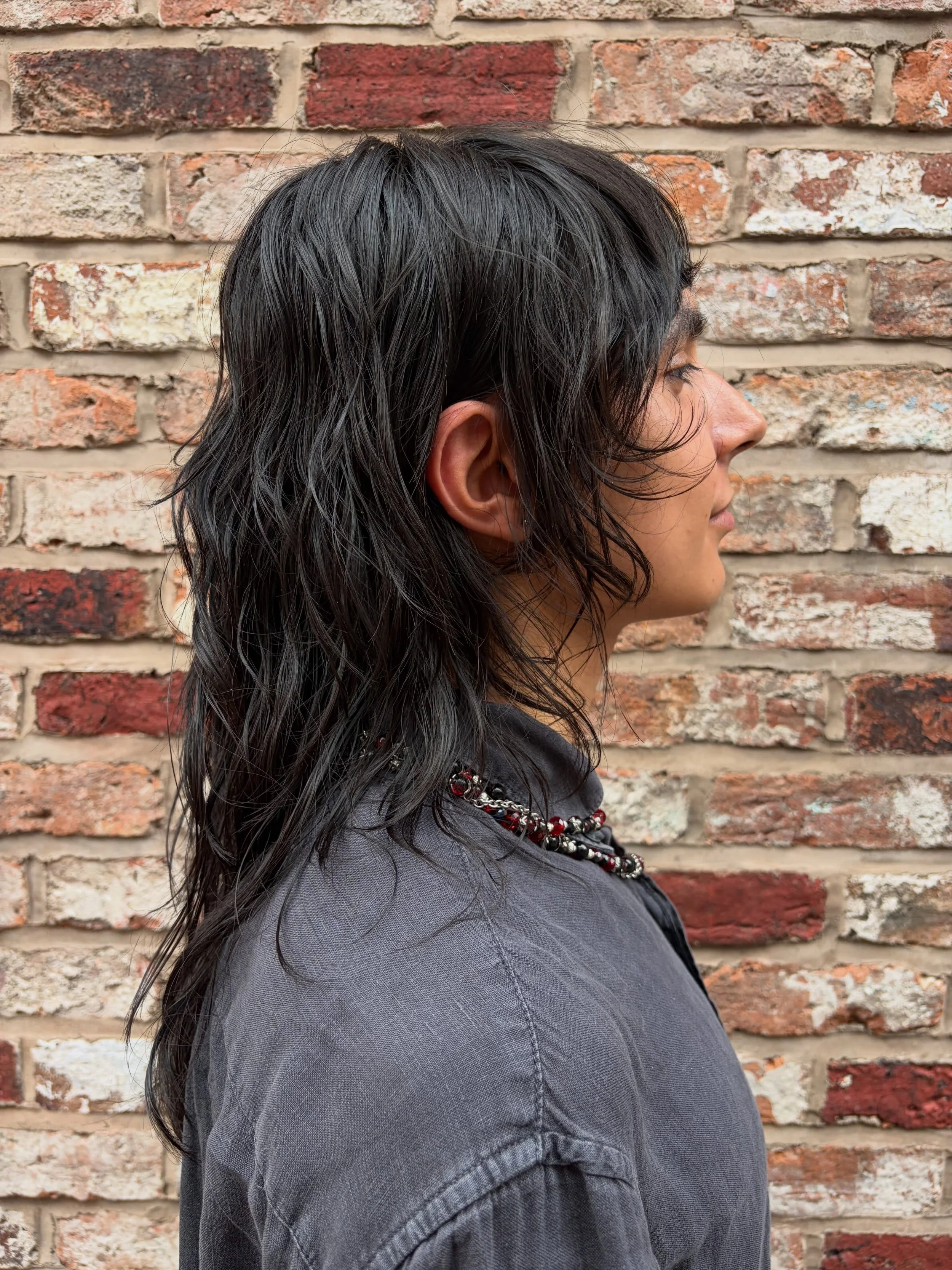 Dark razor-cut mullet shown in profile with layered texture through the back