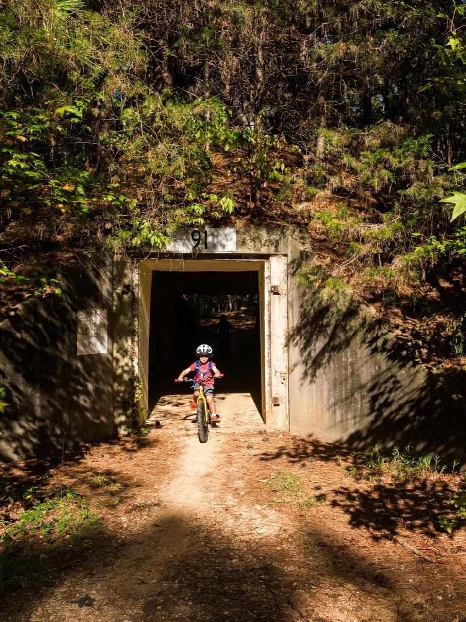 Child riding a bicycle through a tunnel in a forested area.