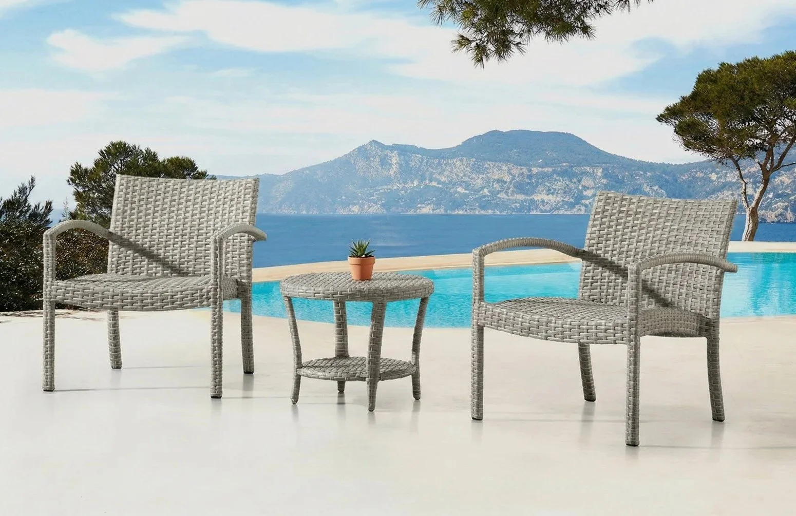 Two wicker chairs with a small table and a potted plant, overlooking a swimming pool and a scenic view of mountains and water.