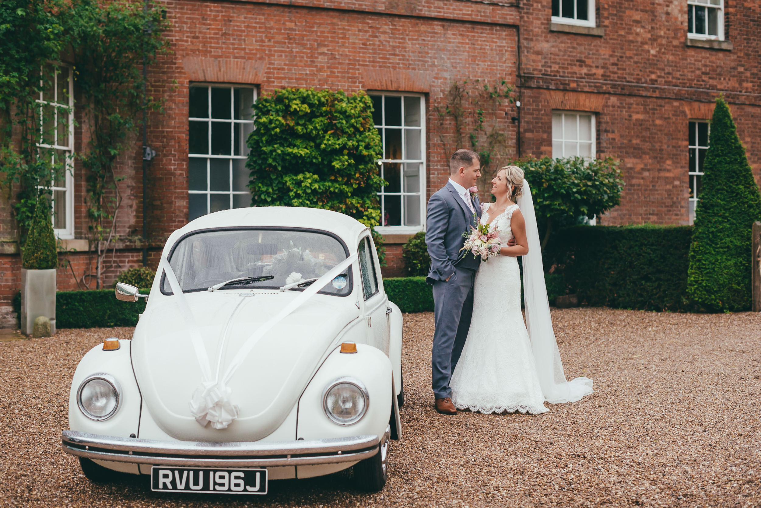 bride and groom standing with the wedding car