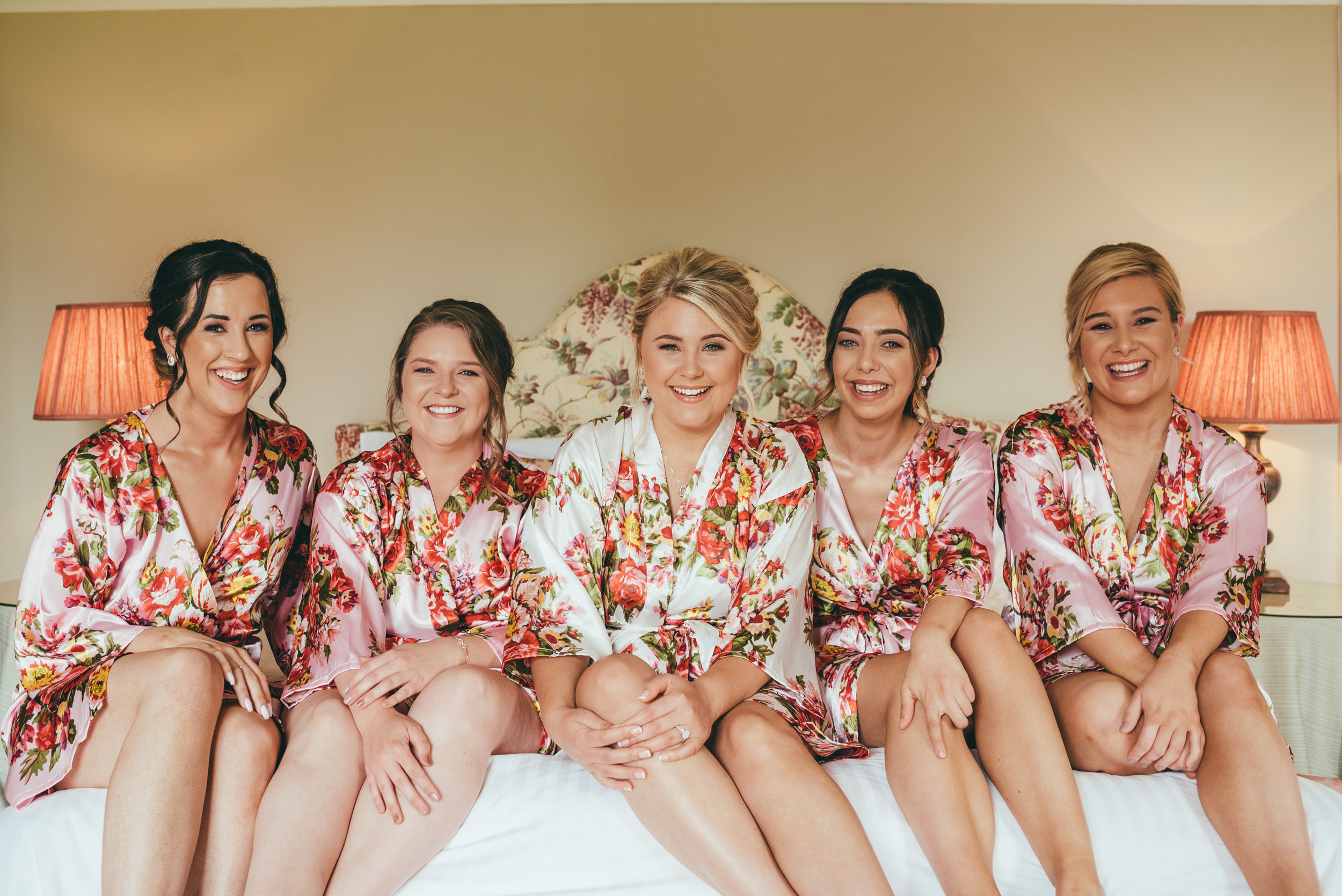 bride and bridesmaids laughing on the bed