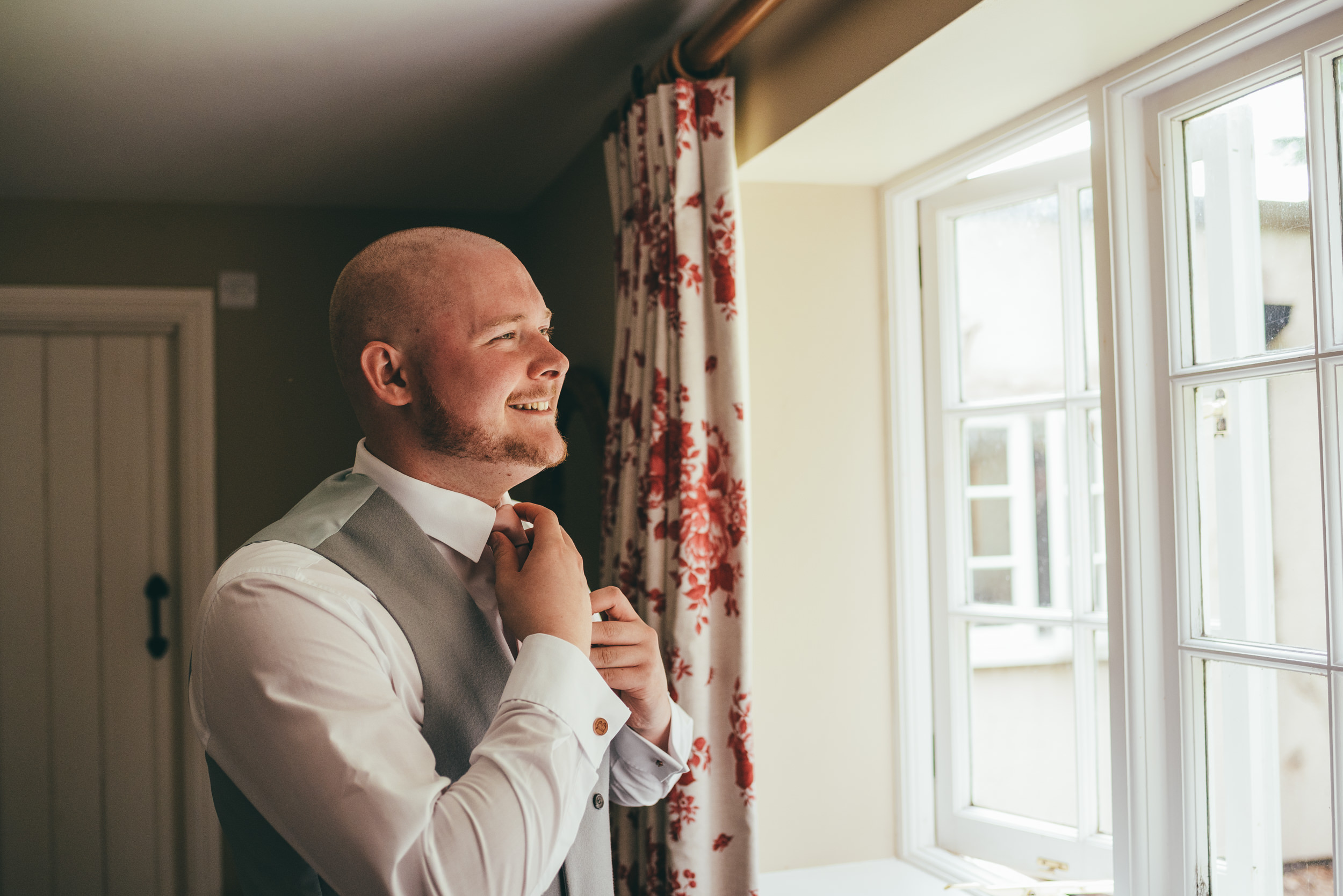 groom adjusting his tie in the window light