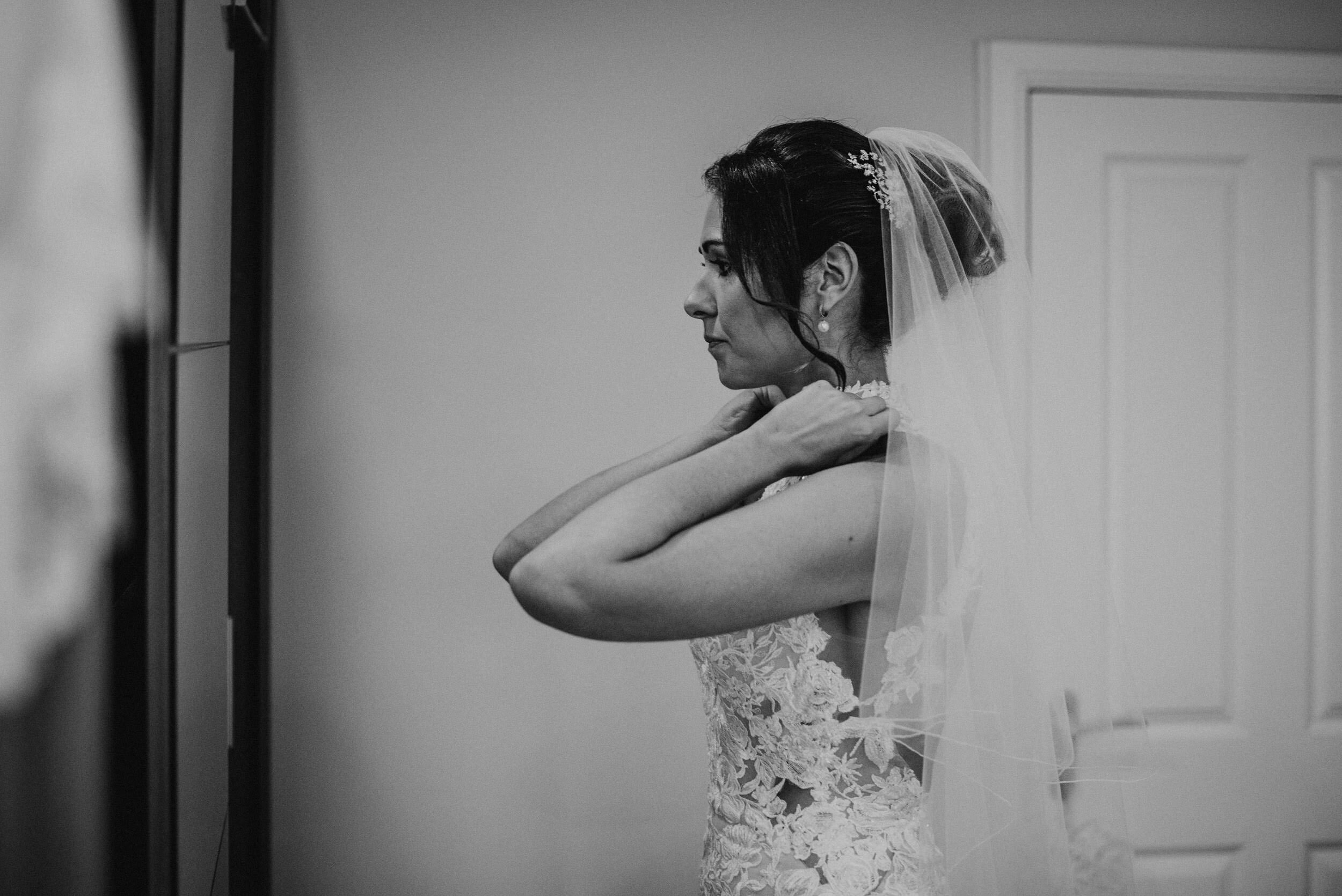 bride putting on her necklace in the mirror