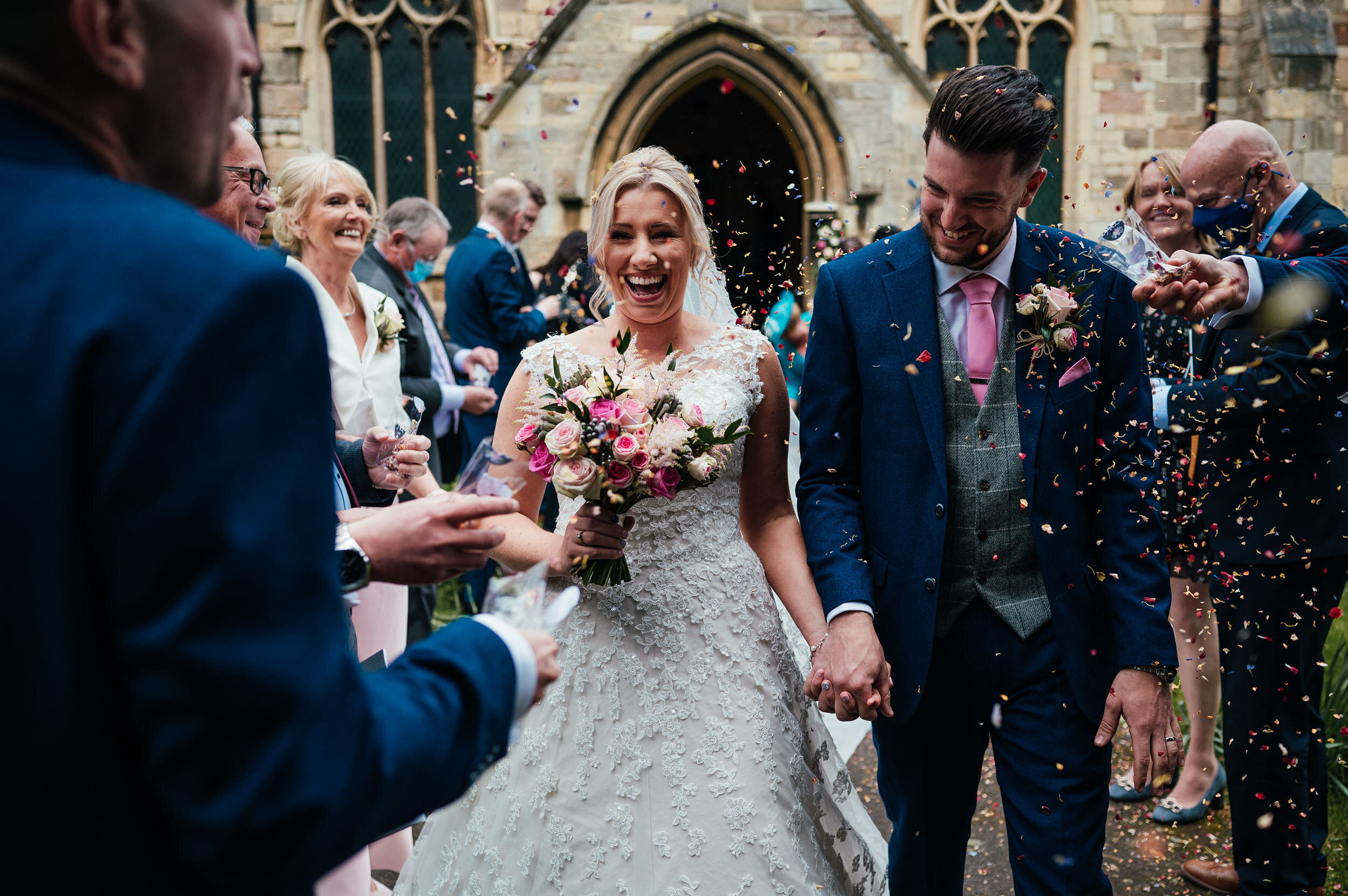 bride and groom laughing during their confetti walk out of church